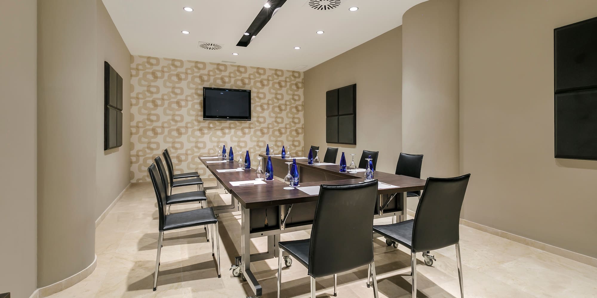 Modern conference room with long table, chairs, TV, and patterned wall.