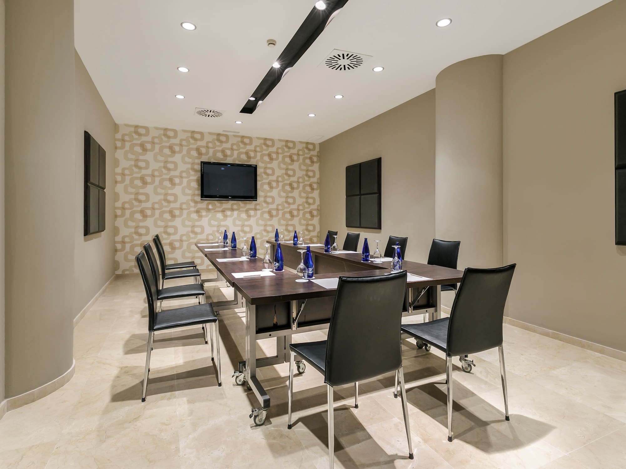 Modern hotel meeting room with dark table, chairs, and TV screen.
