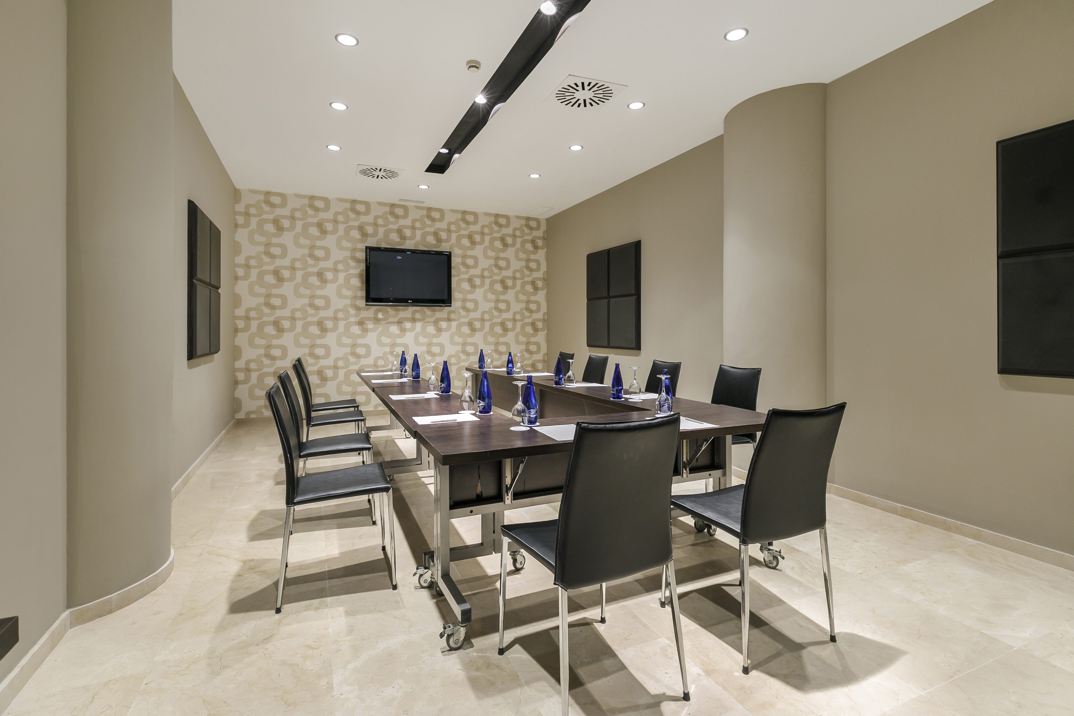 Modern hotel meeting room with dark table, chairs, and TV screen.