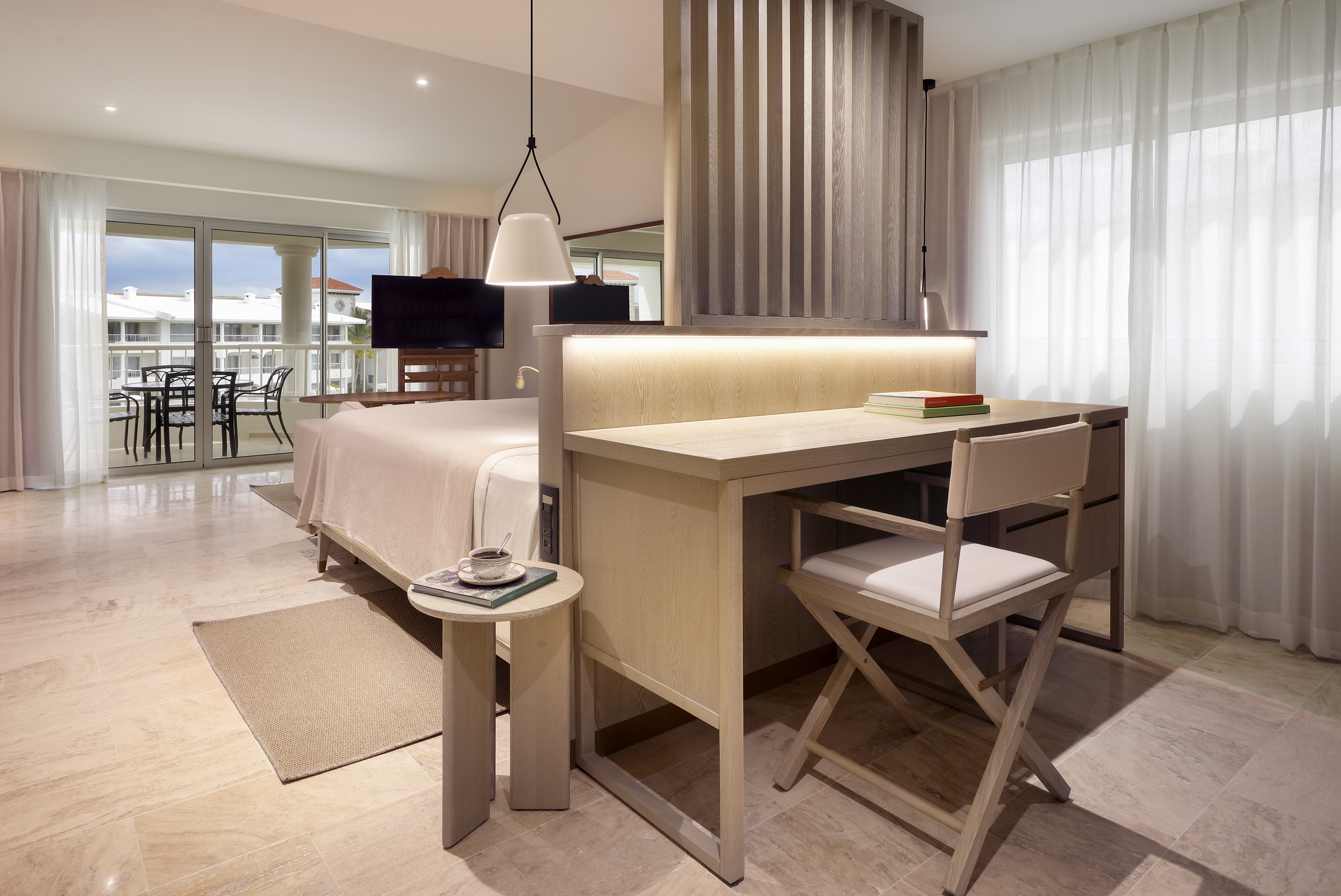 Modern hotel suite with balcony, bed, desk, and neutral light wood decor.