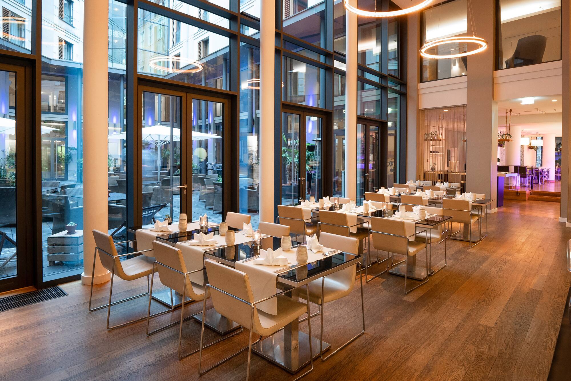 Contemporary restaurant interior with set tables and view of outdoor patio.