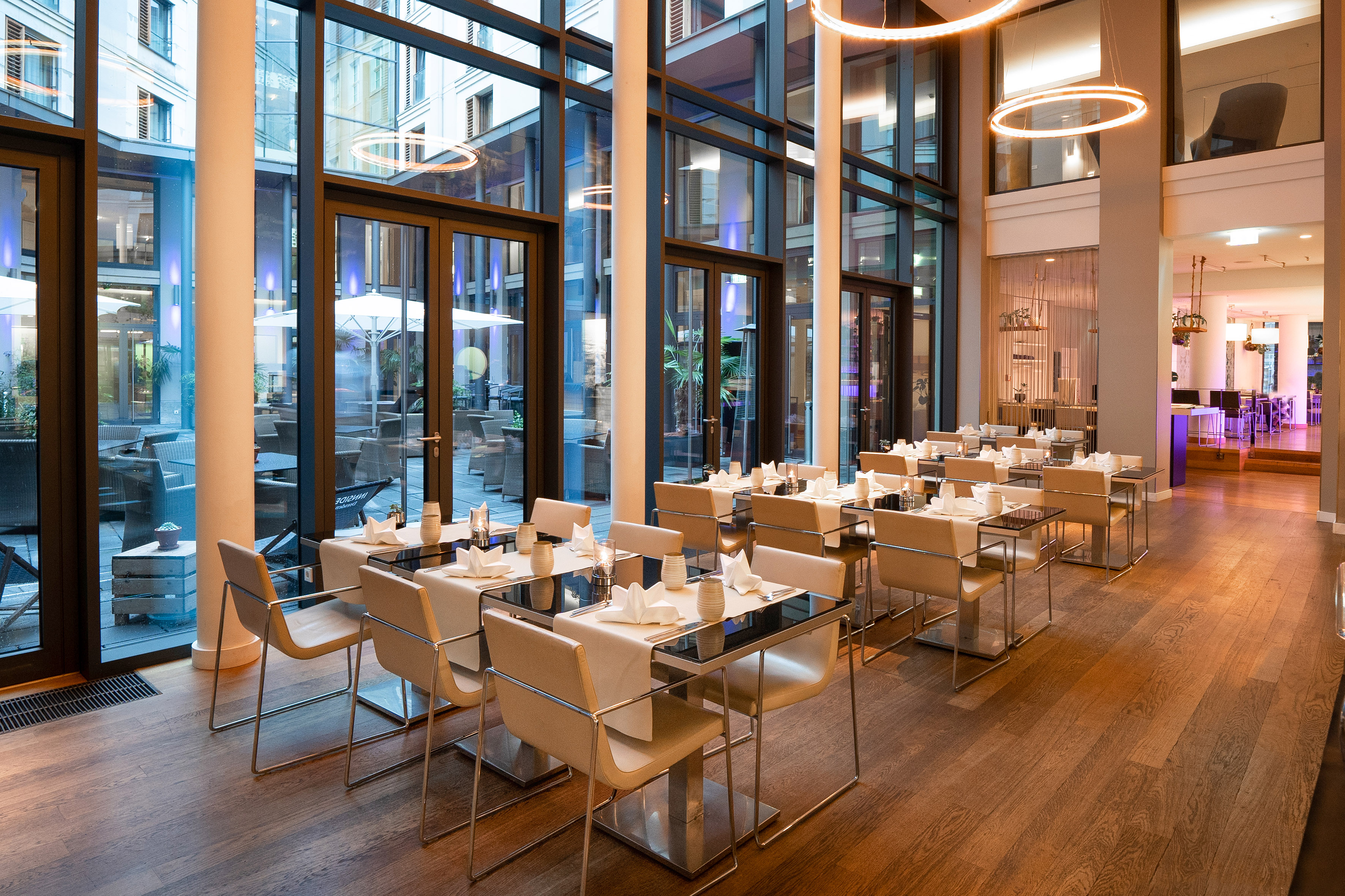 Contemporary restaurant interior with set tables and view of outdoor patio.