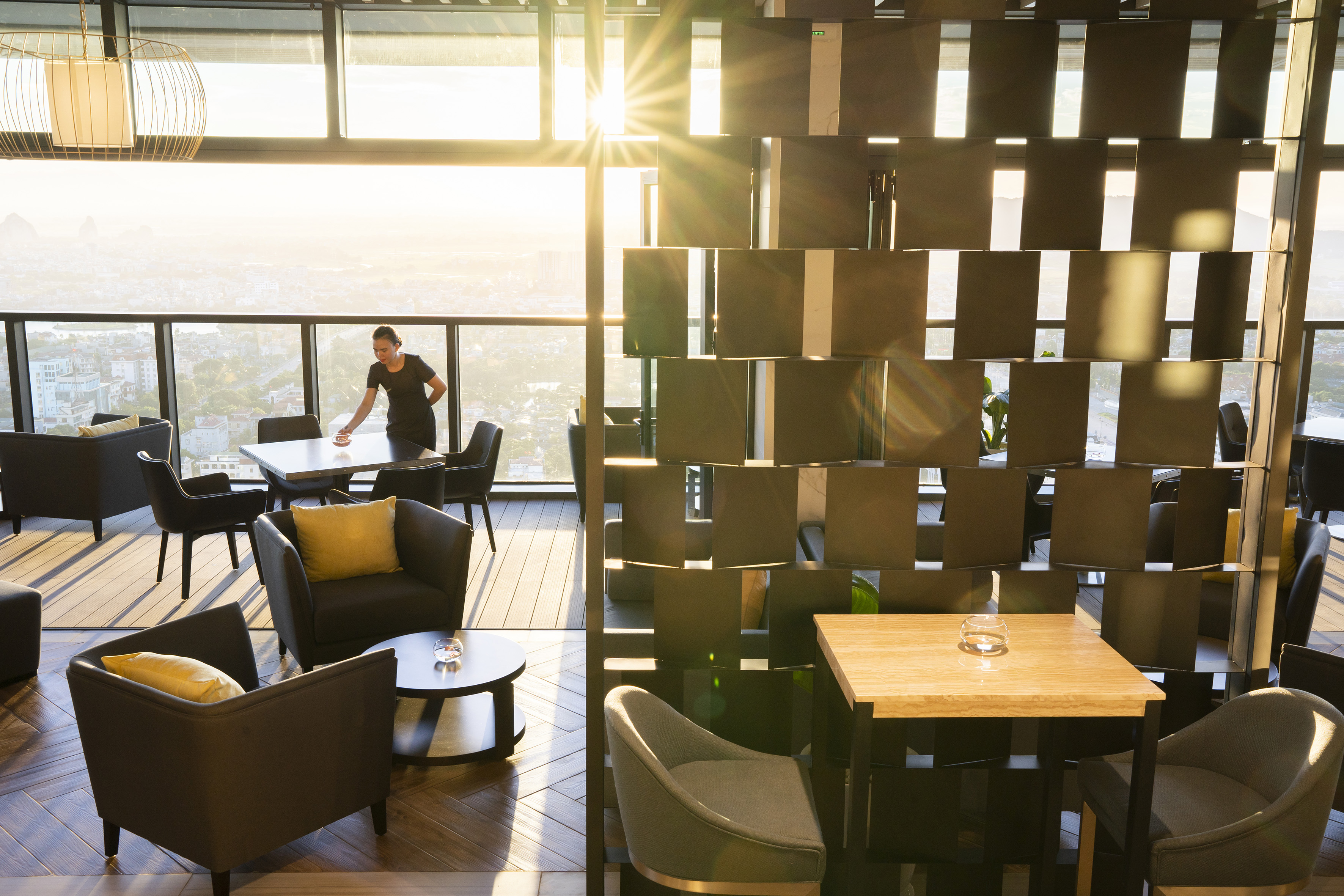 Modern rooftop lounge with sunset city view, staff preparing tables.
