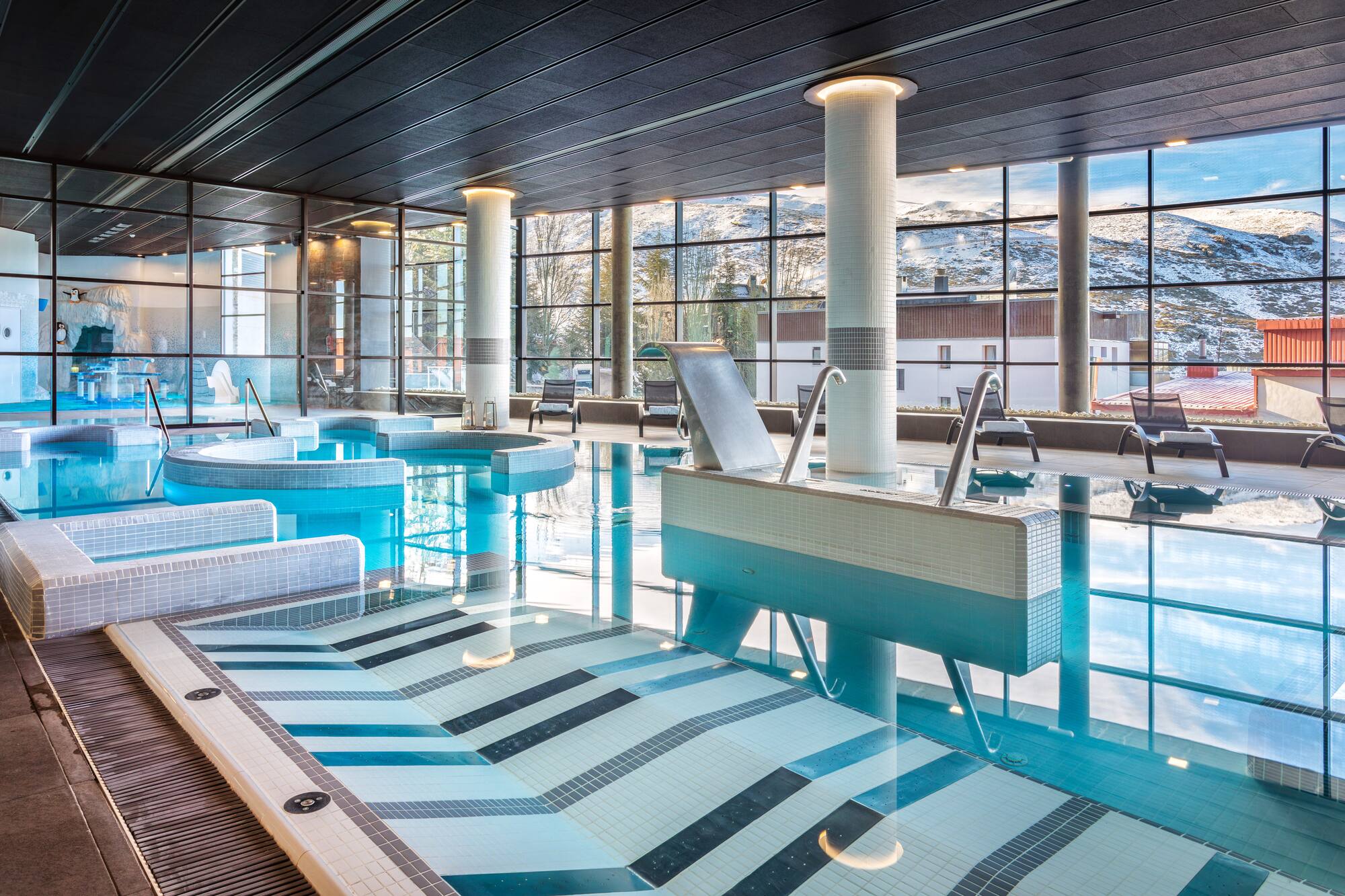Indoor spa pool with panoramic snowy mountain views and modern design.