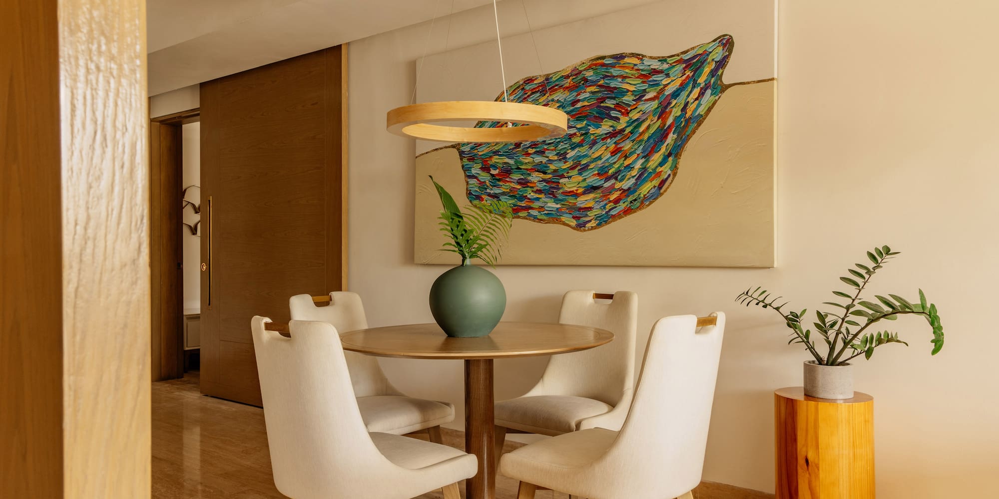 Modern dining room: round table, four chairs, colorful abstract art, minimalist decor.