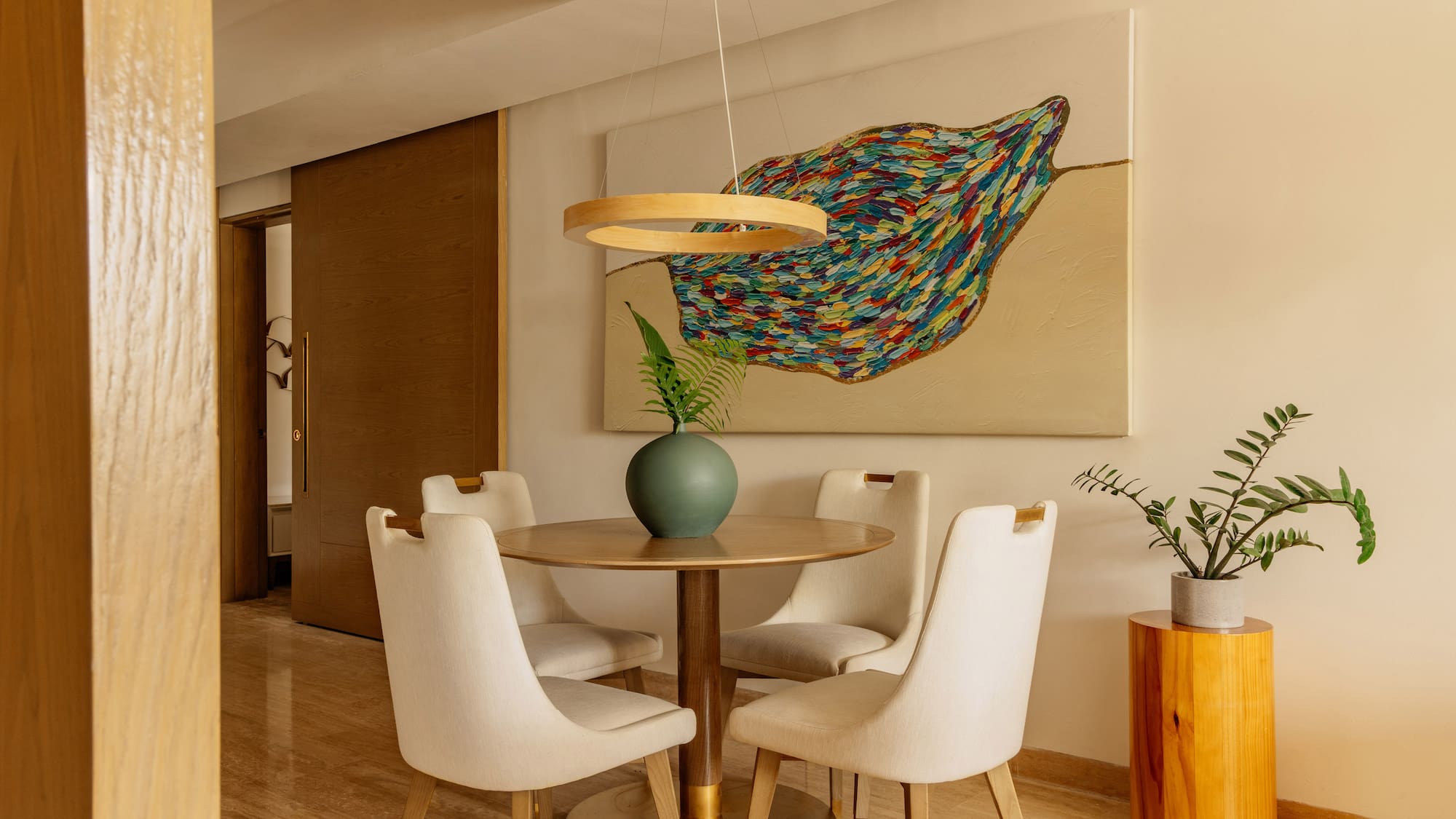 Modern dining room: round table, four chairs, colorful abstract art, minimalist decor.