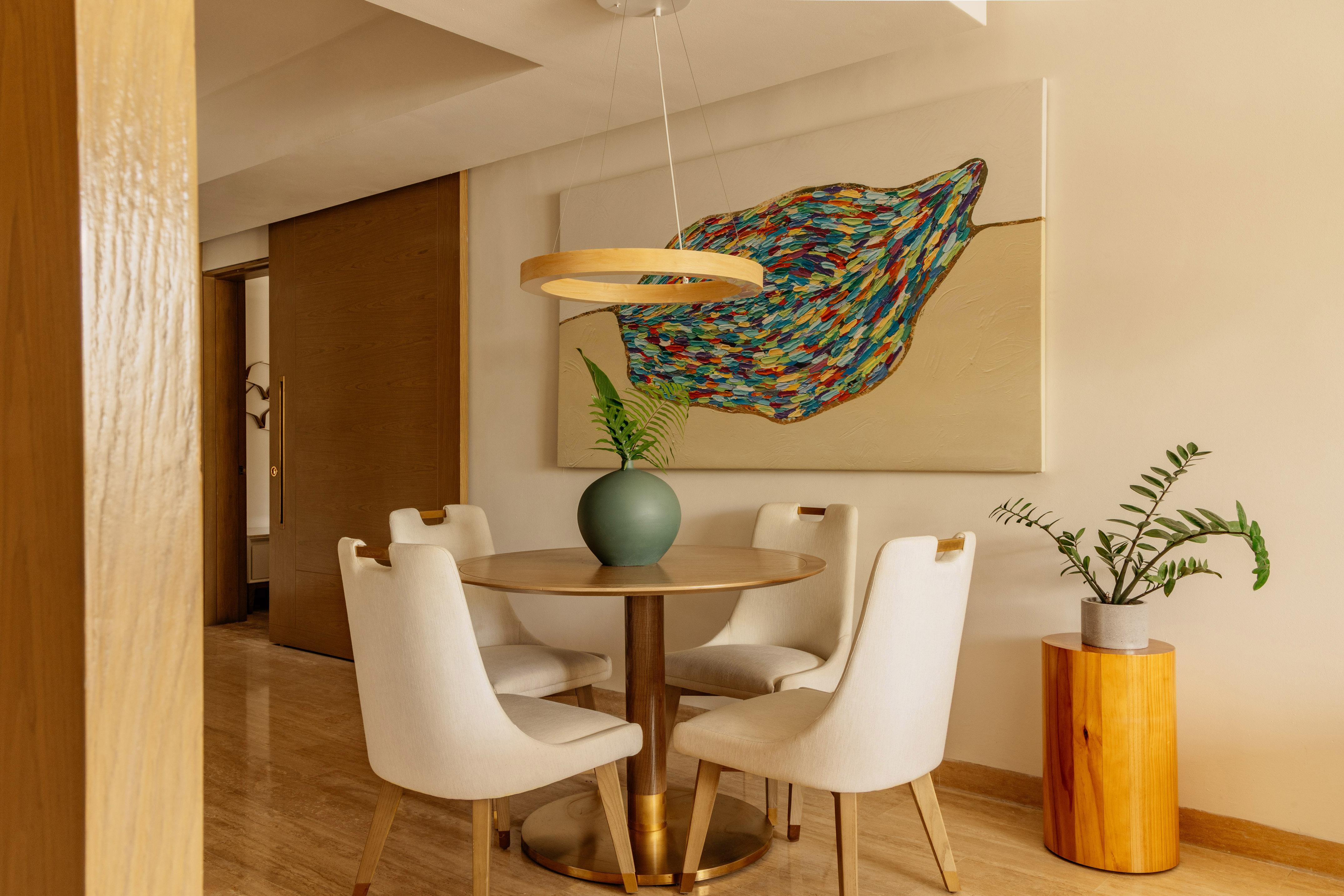 Modern dining room: round table, four chairs, colorful abstract art, minimalist decor.