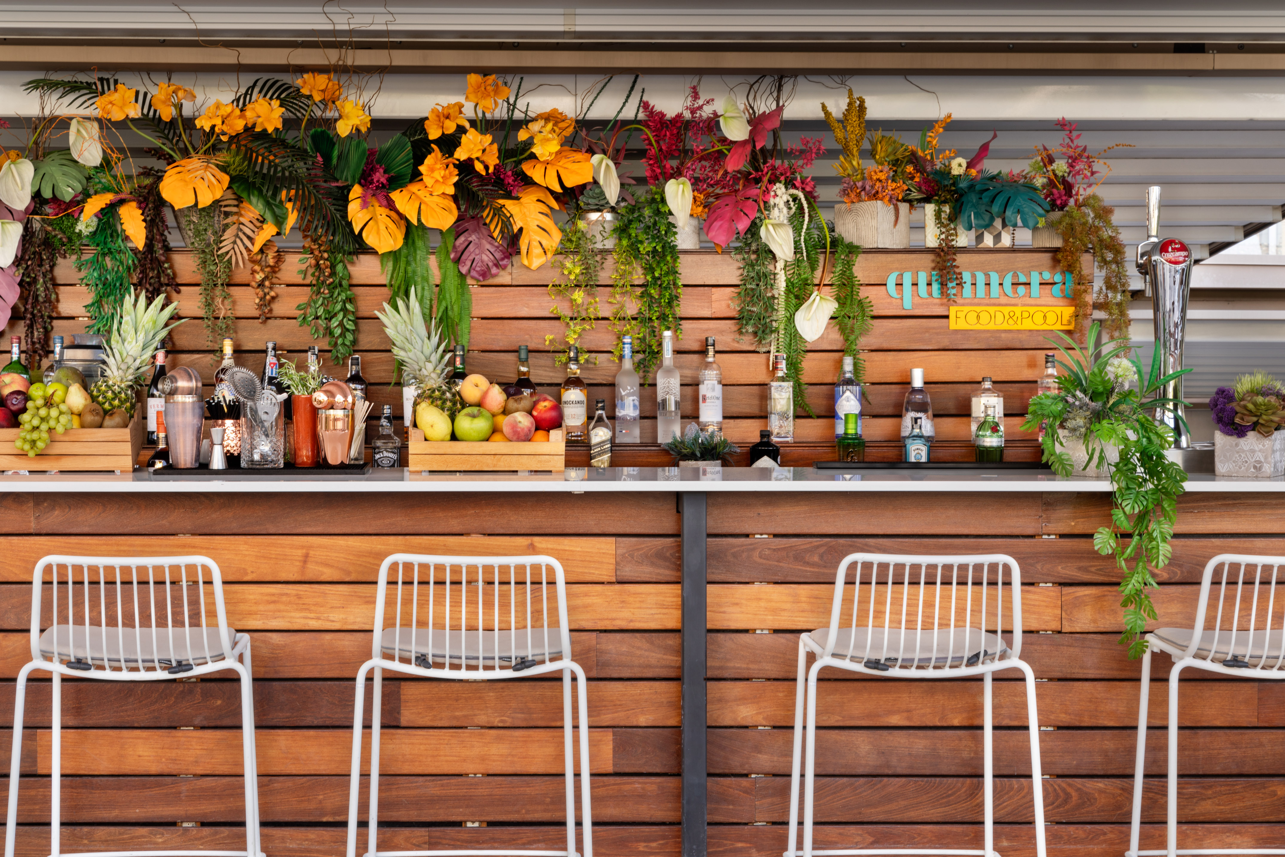 Tropical poolside bar with liquor, fresh fruit, and white bar stools.
