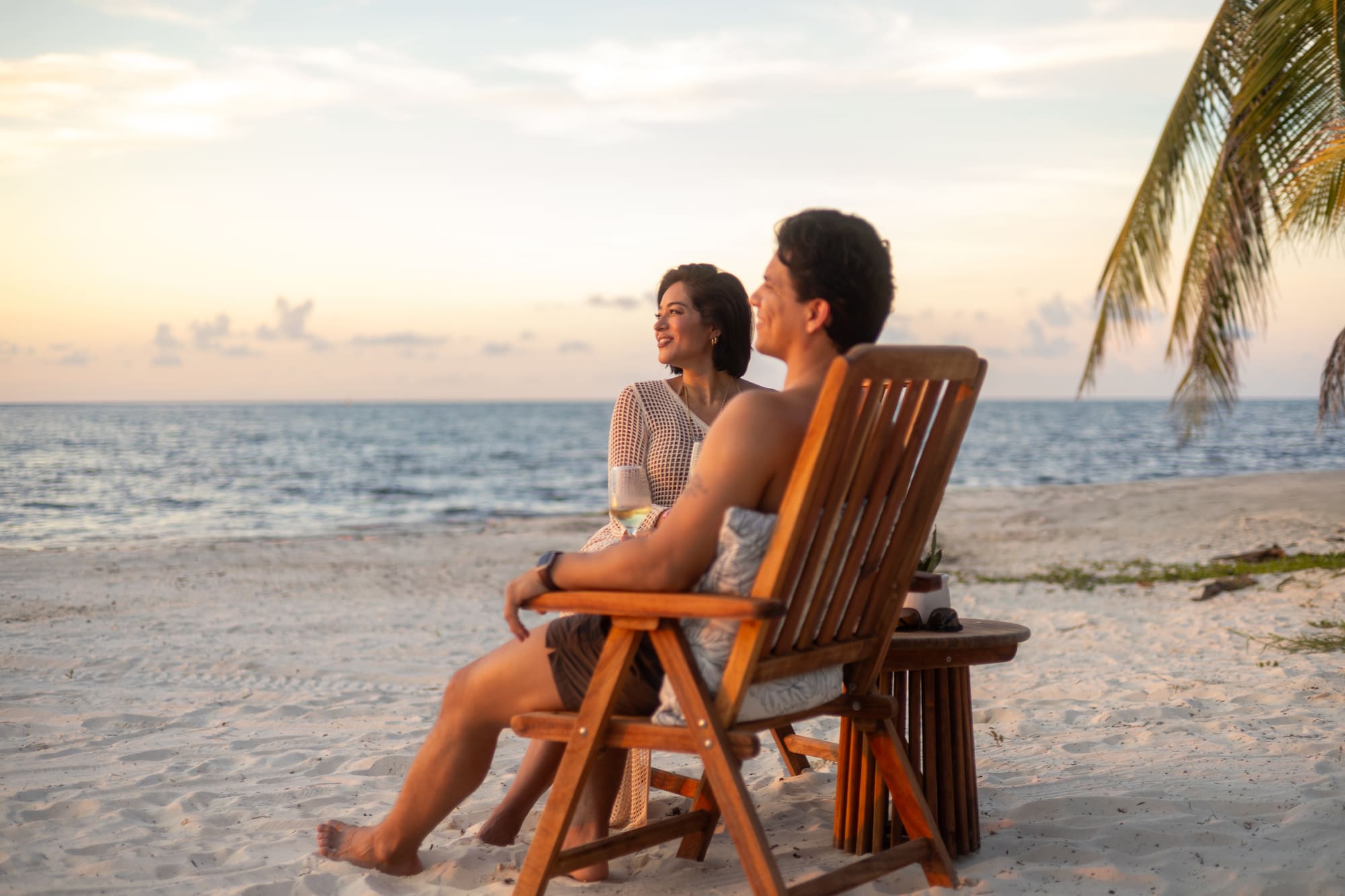 Pareja disfrutando el atardecer en la playa, con mar y palmeras.
