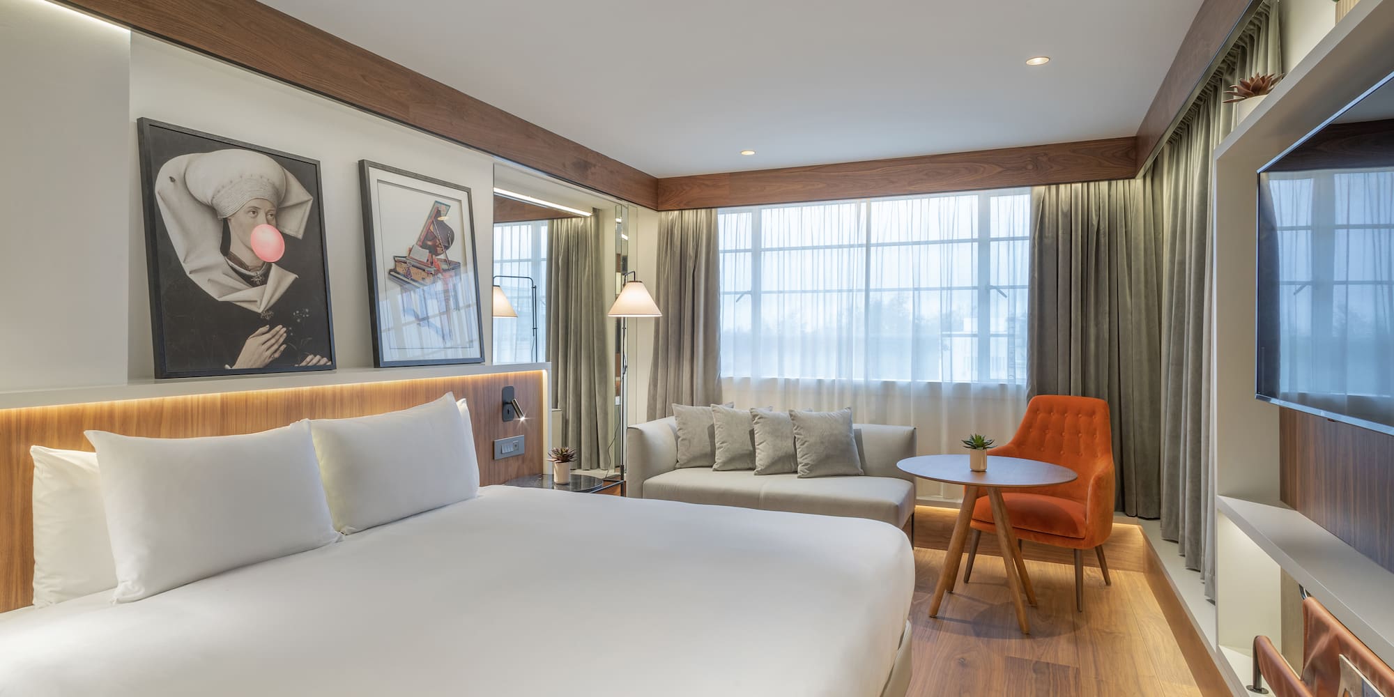 Modern hotel room with king bed, sitting area, large window, and wood details.
