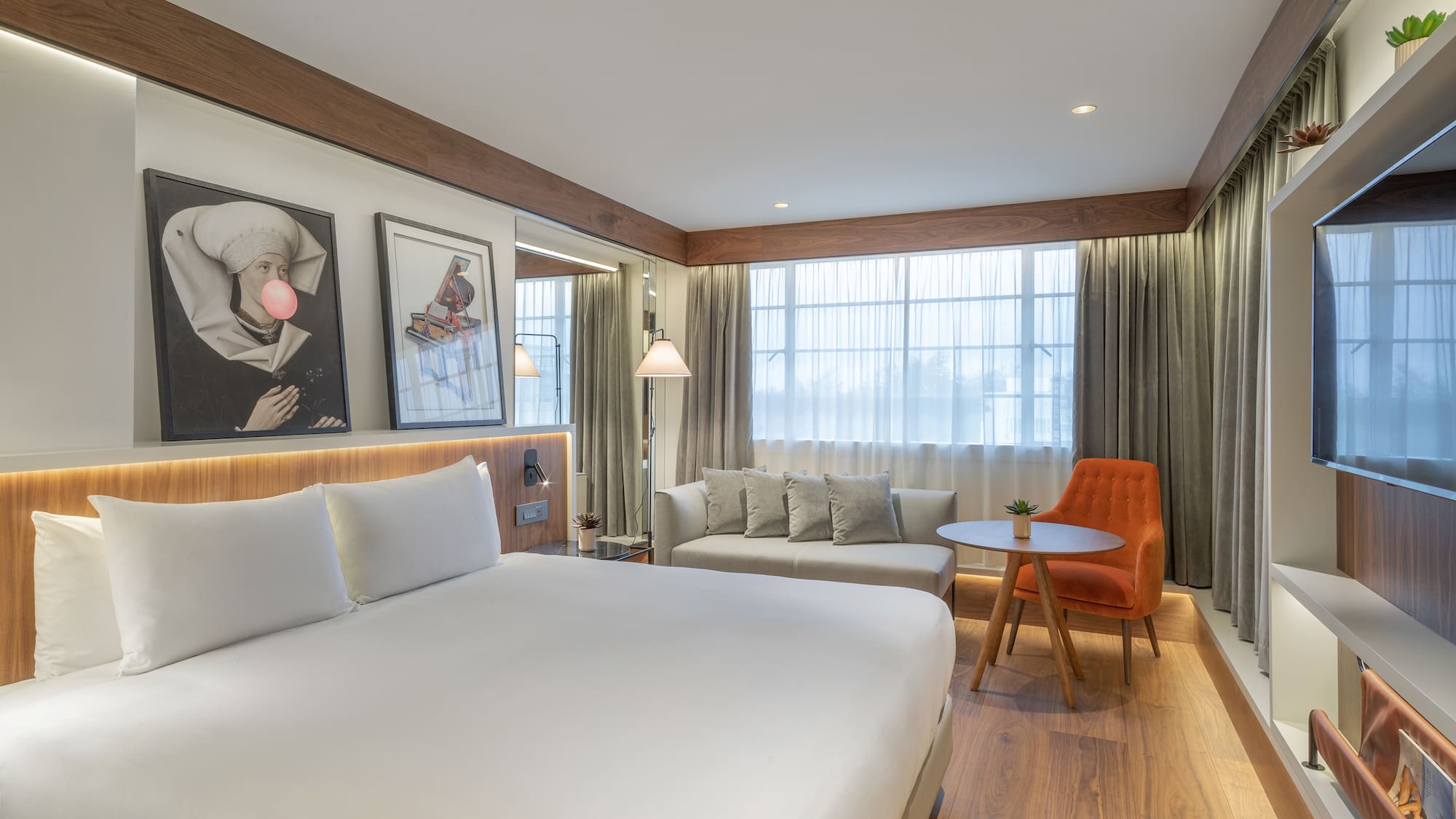 Modern hotel room with king bed, sitting area, large window, and wood details.