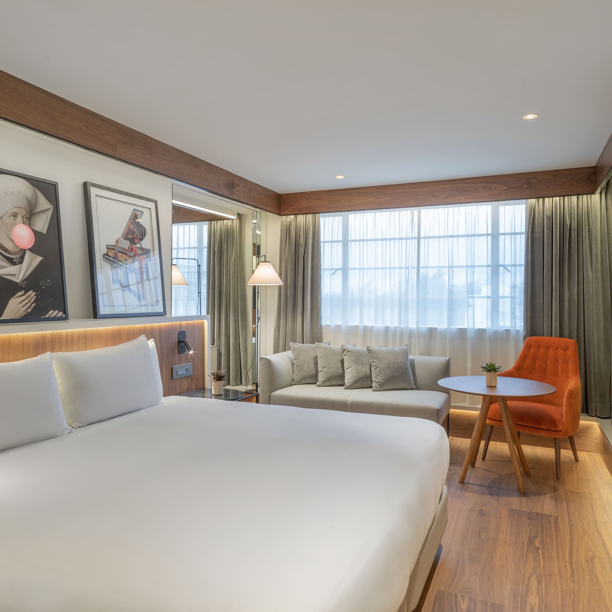 Modern hotel room with king bed, sitting area, large window, and wood details.