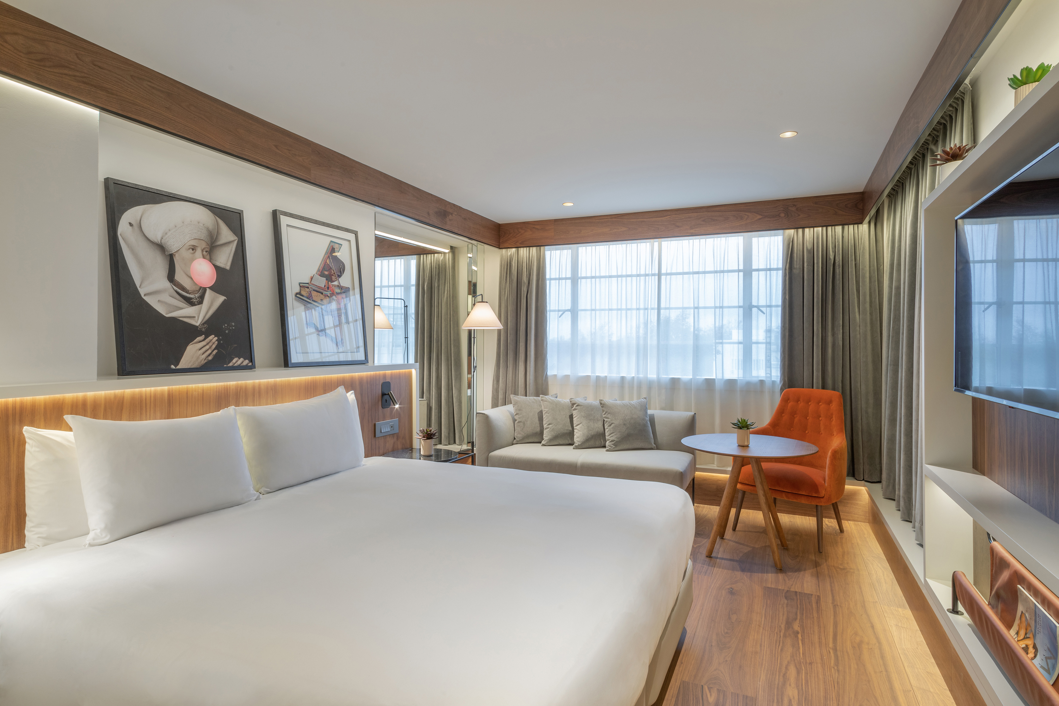 Modern hotel room with king bed, sitting area, large window, and wood details.