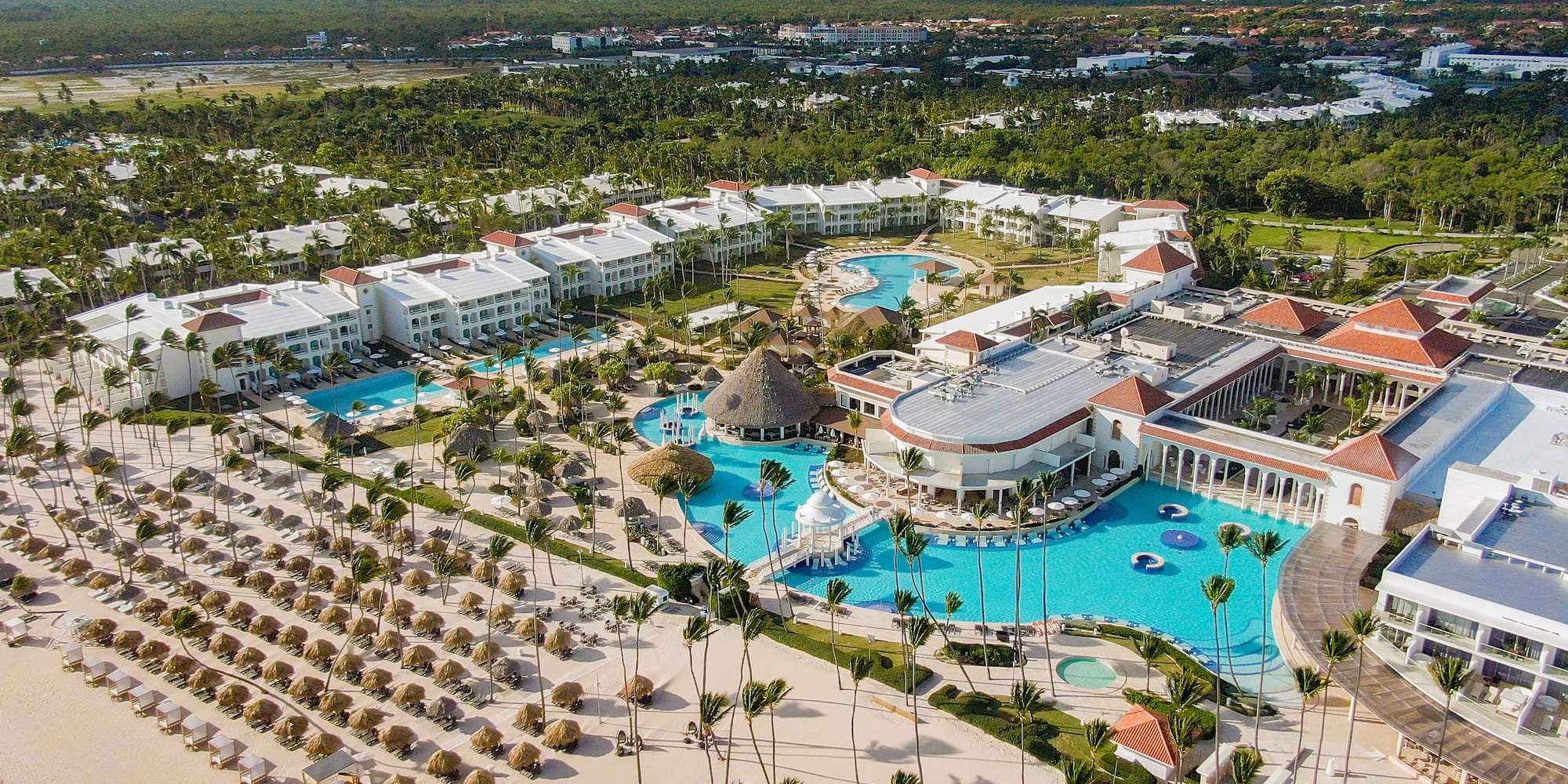 Aerial view of luxury tropical resort, multiple pools, sandy beach, palm trees.