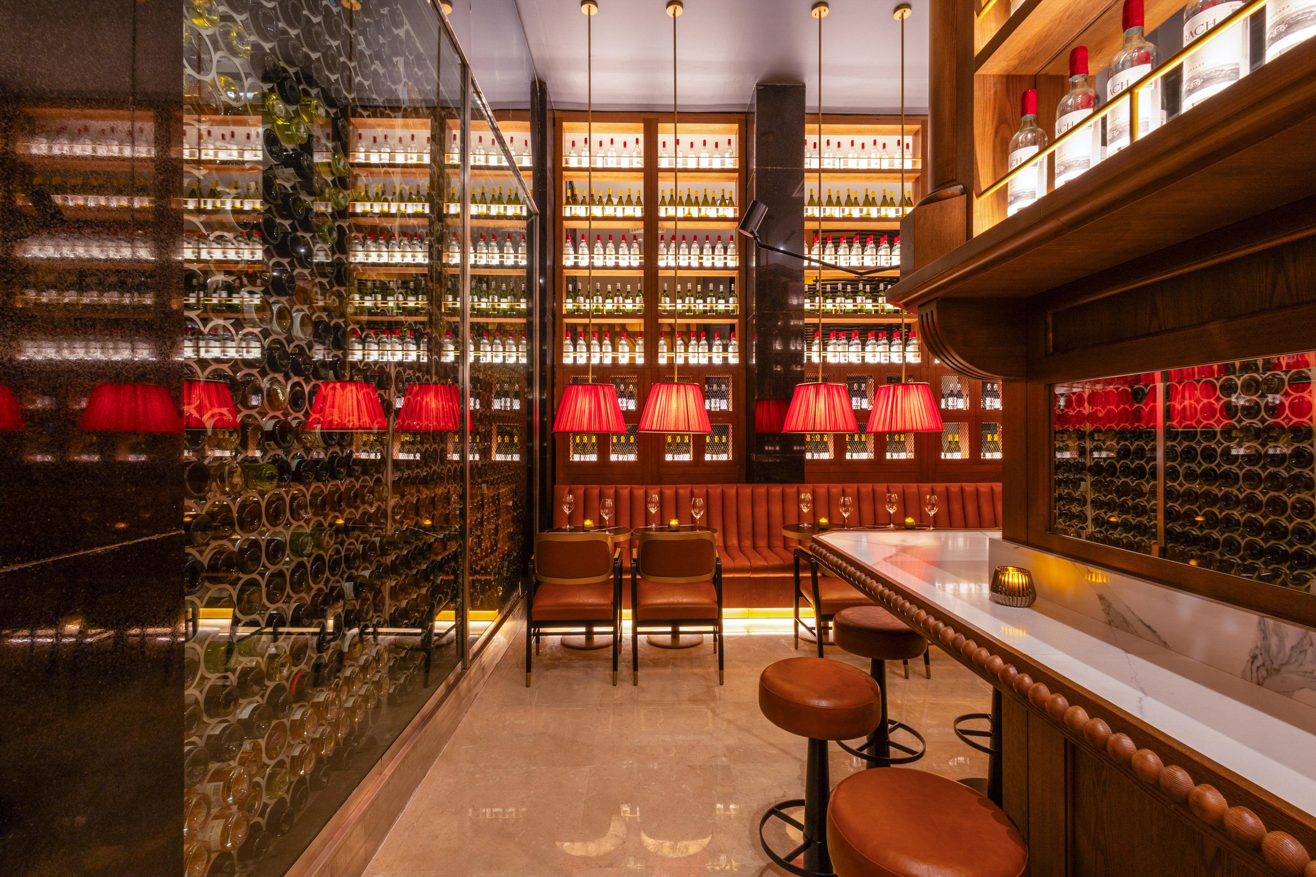 Luxury wine bar with glass cellar, red lights, marble bar, and leather seating.