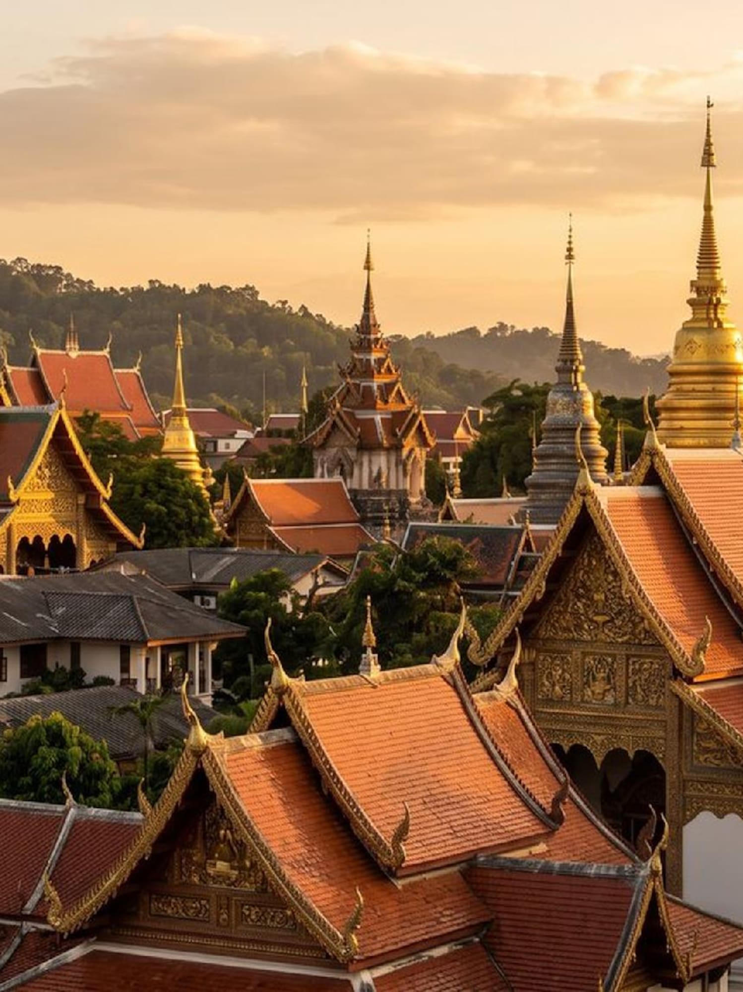 Golden spires and red-tiled roofs of Thai temples at sunset.