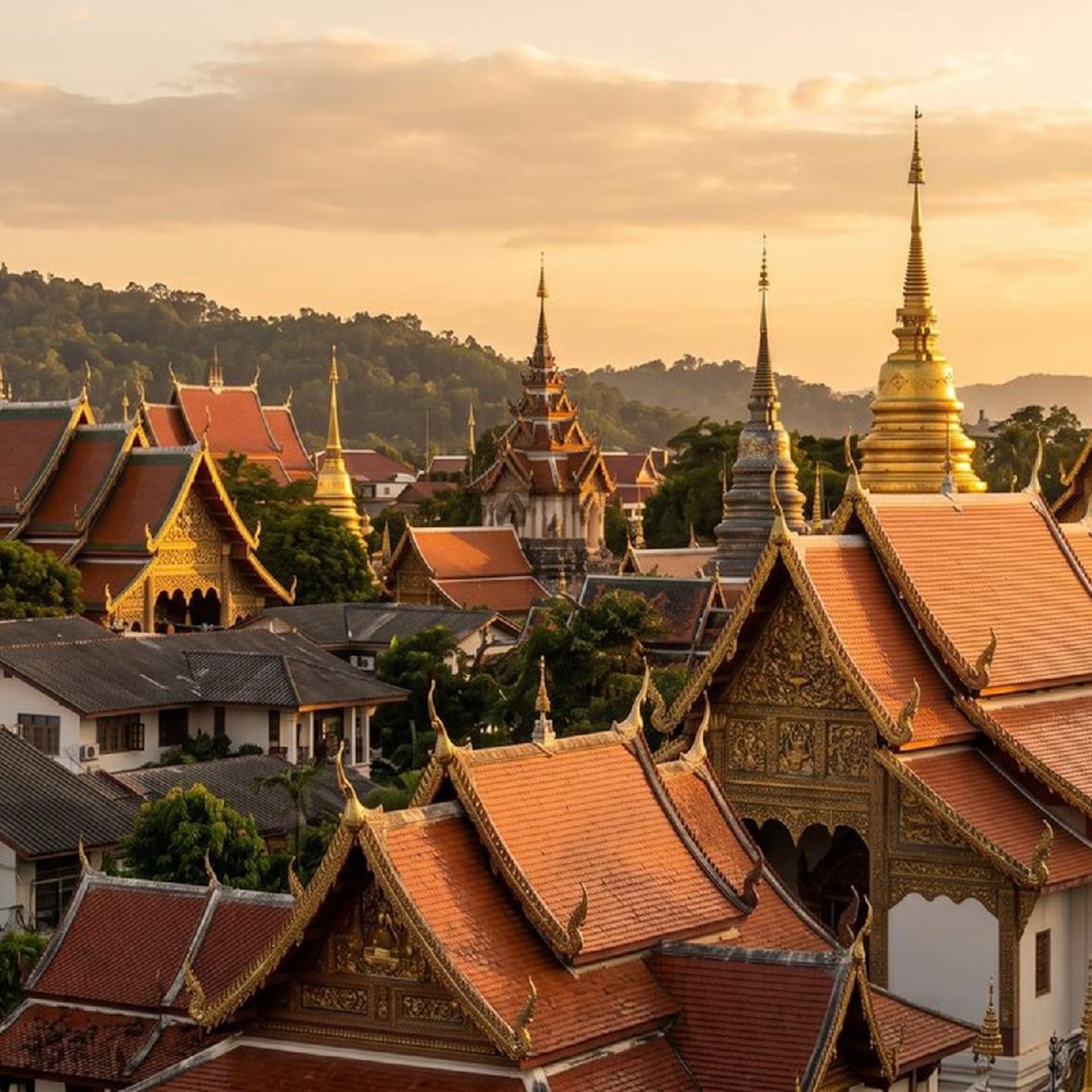 Golden spires and red-tiled roofs of Thai temples at sunset.