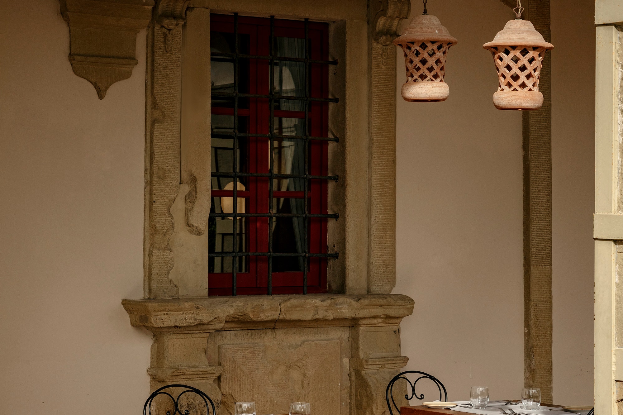 Al fresco dining patio, wrought-iron chairs, red window, terracotta lanterns.