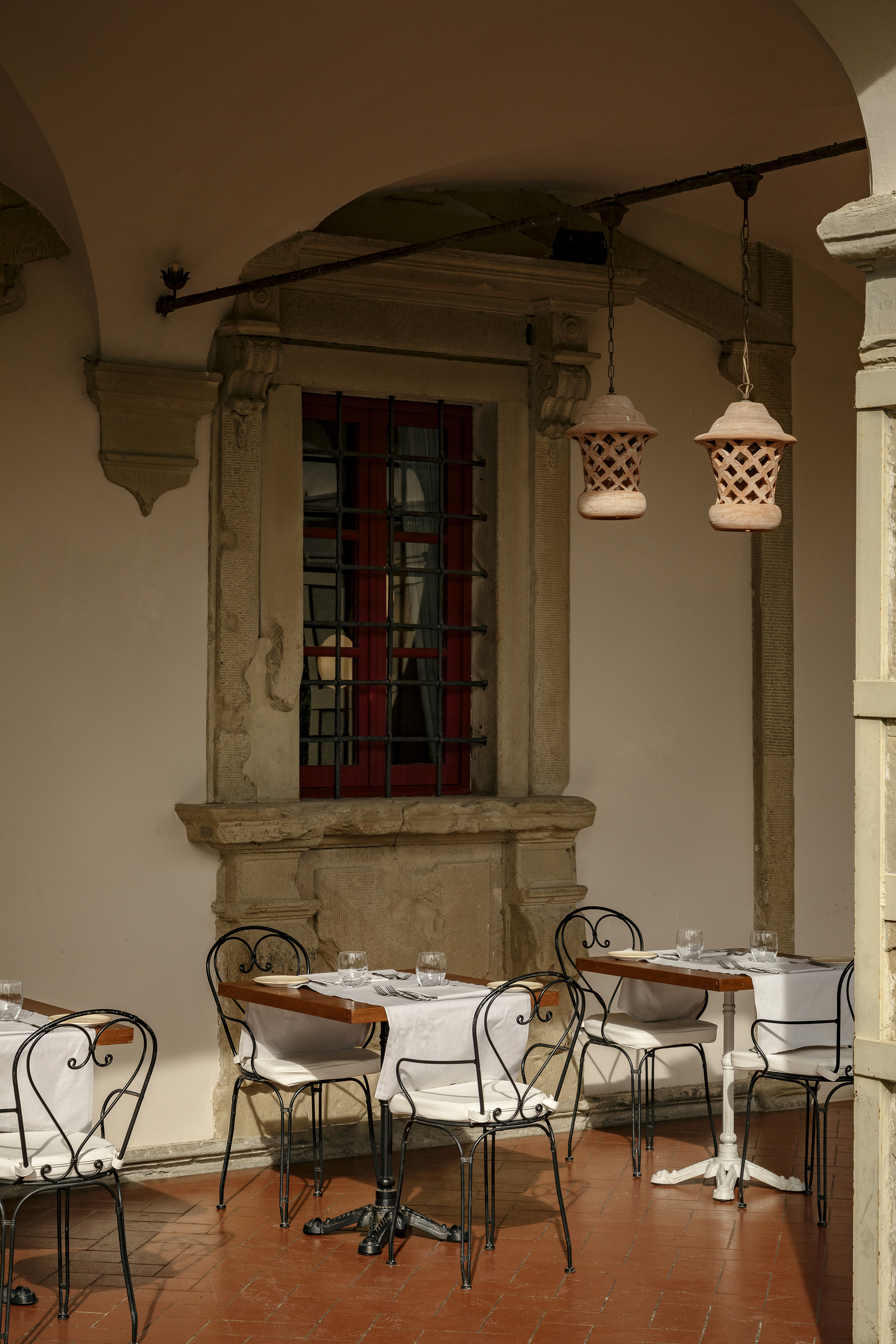 Al fresco dining patio, wrought-iron chairs, red window, terracotta lanterns.