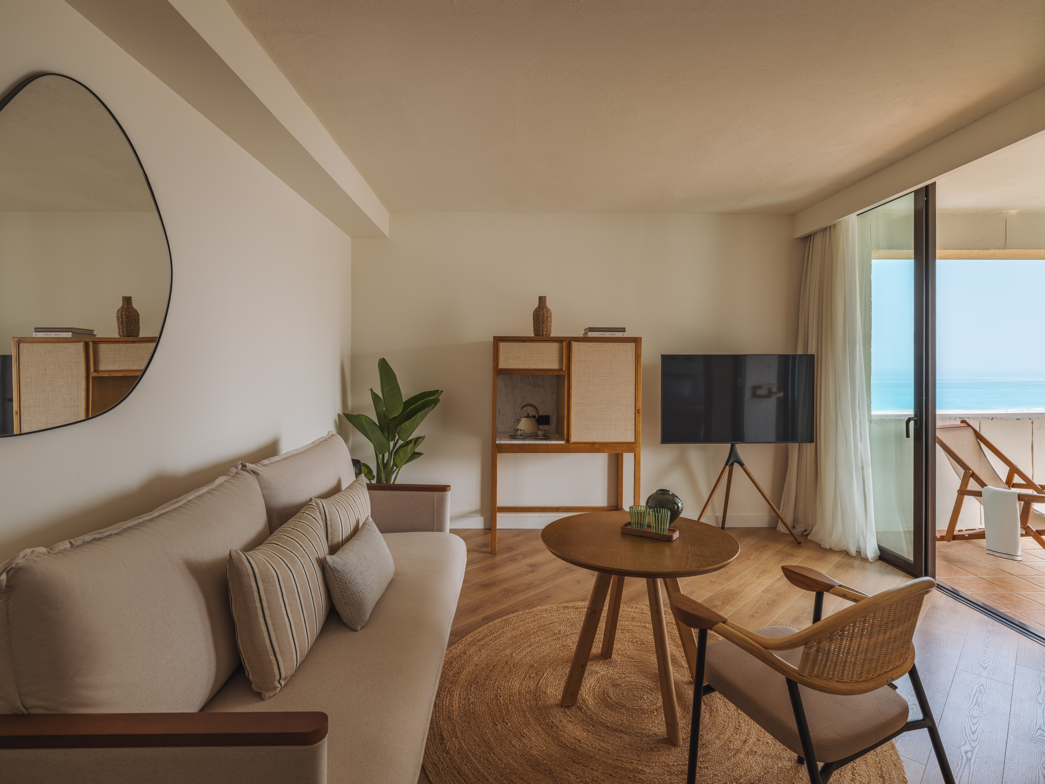 Coastal living room with neutral sofa, wooden table, and ocean view balcony.