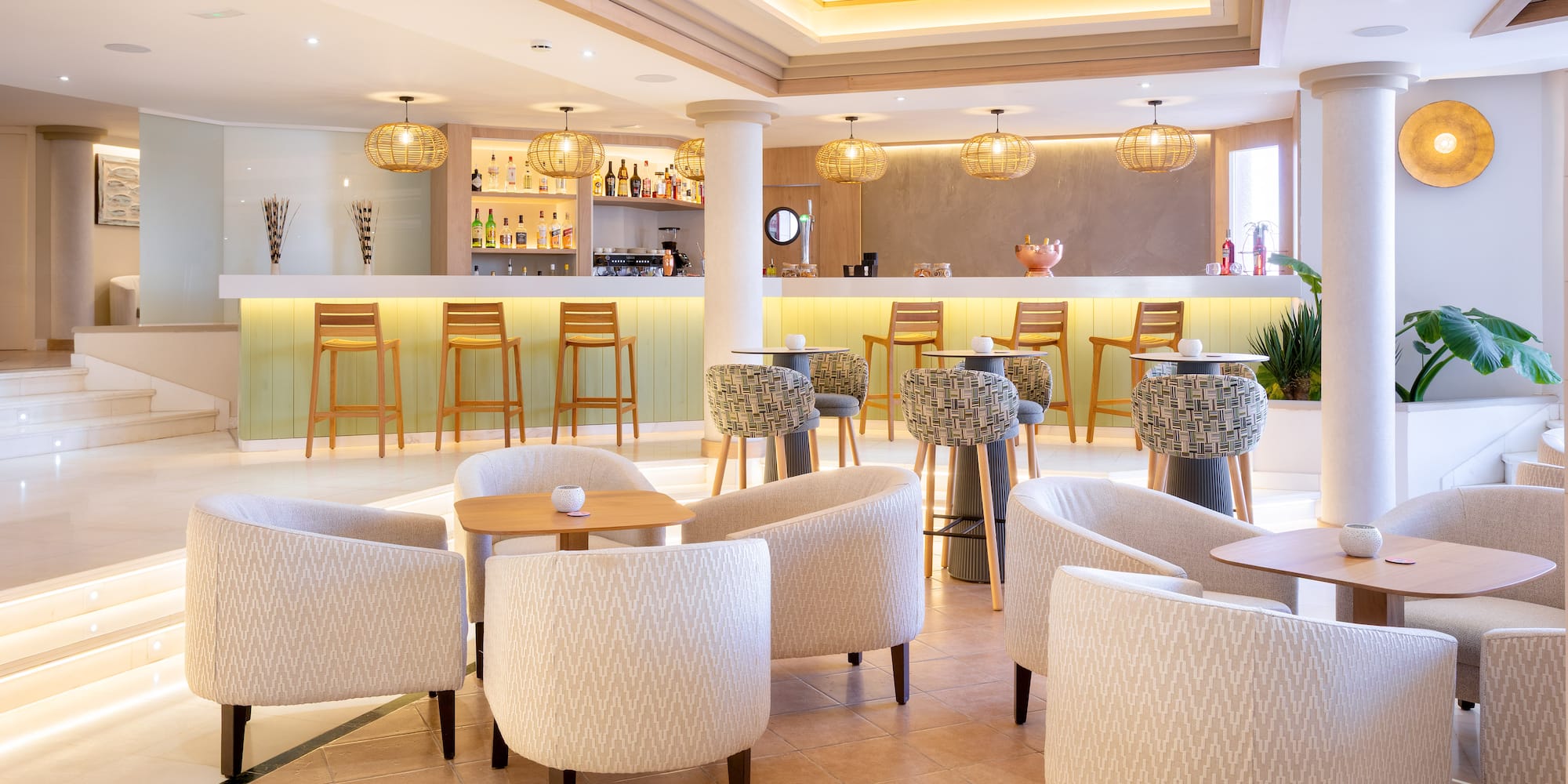 Modern hotel bar and lounge with stylish armchairs, bar stools, and warm lighting.