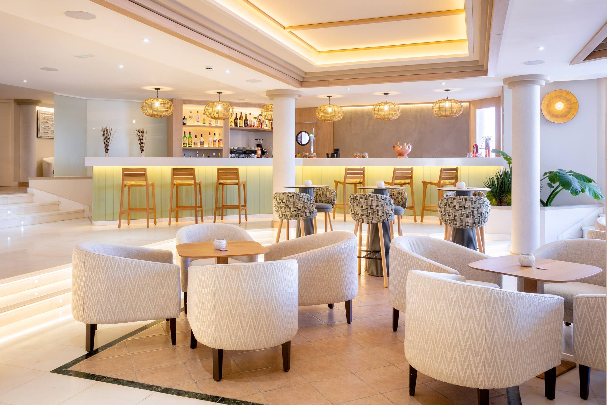 Modern hotel lobby bar with lounge chairs, bar stools, and ambient lighting.