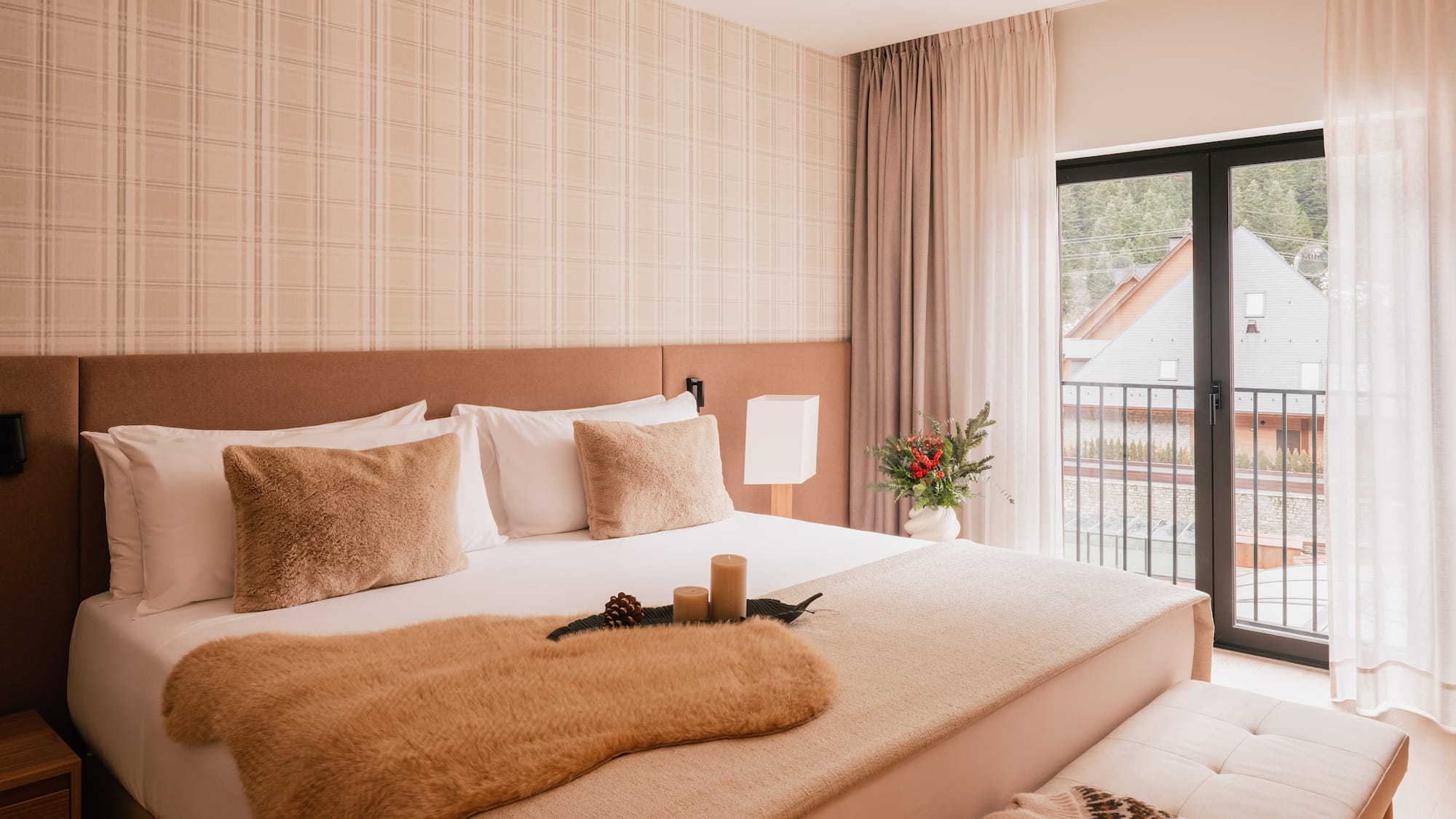 Cozy hotel bedroom with neutral decor, fur throw, plaid wall, and balcony view.