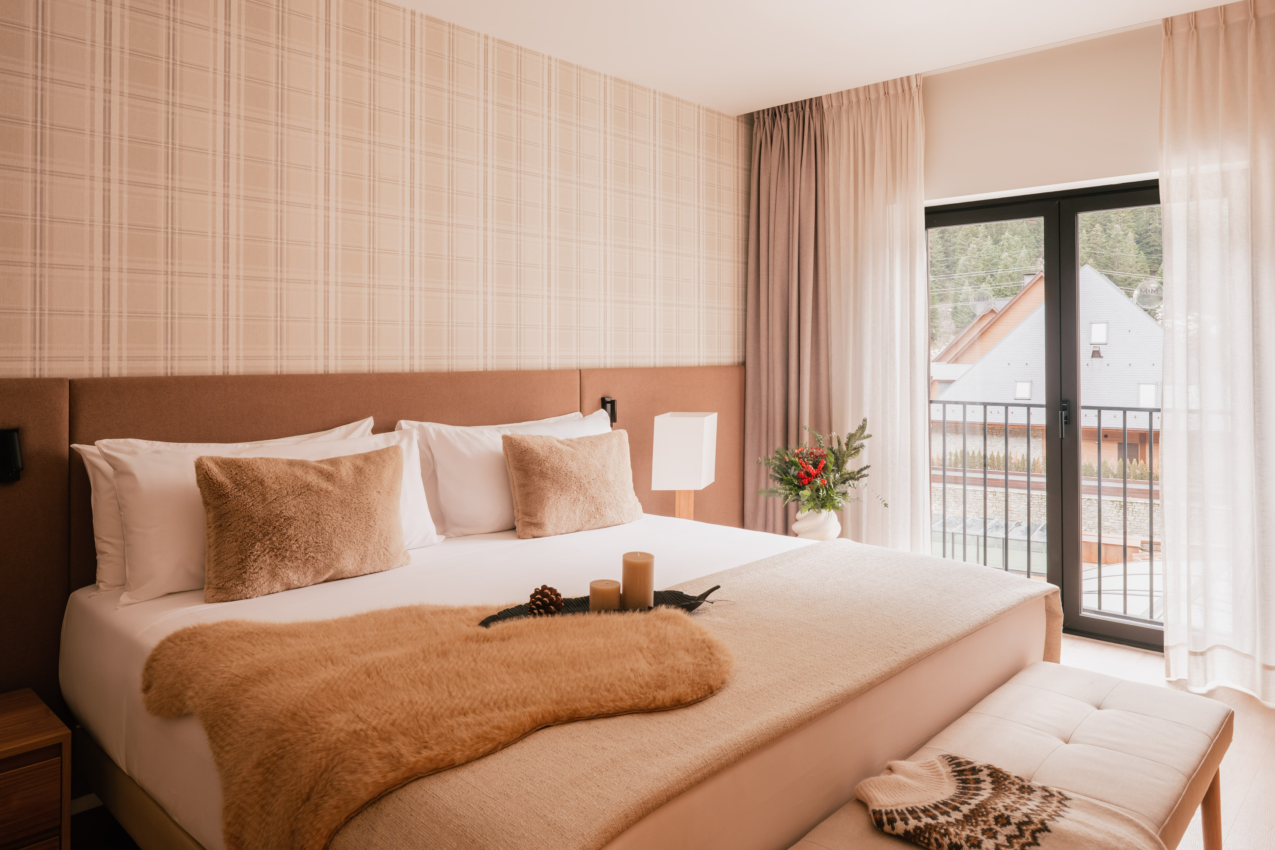 Cozy hotel bedroom with neutral decor, fur throw, plaid wall, and balcony view.
