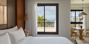 a bed with white sheets and a window overlooking a body of water