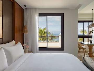 a bed with white sheets and a window overlooking a body of water