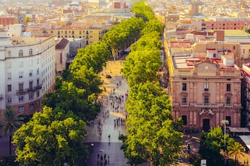 a group of people walking on a sidewalk with trees with La Rambla, Barcelona in the background