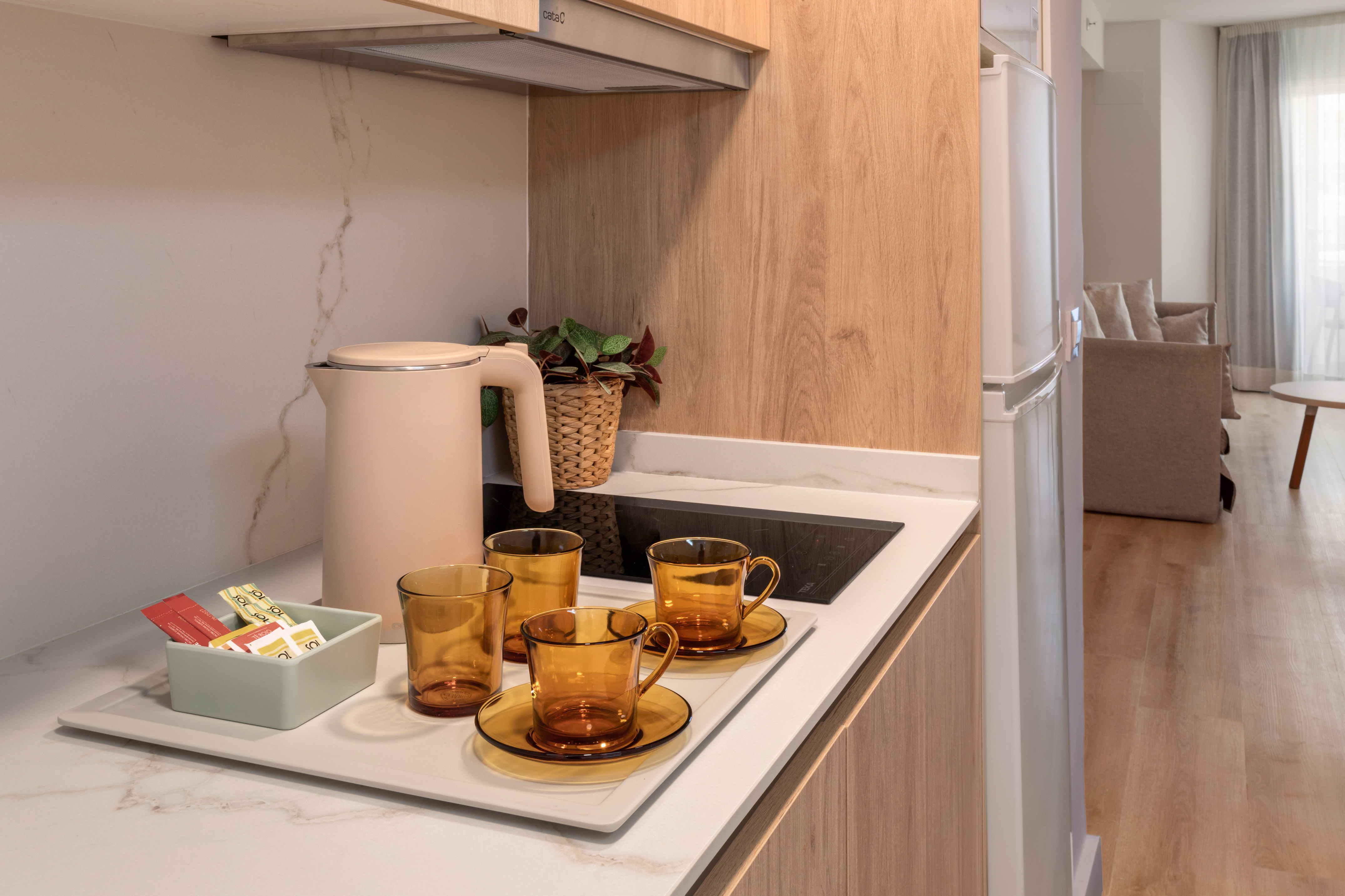 Modern kitchenette with kettle, amber tea set, and tea sachets on marble.