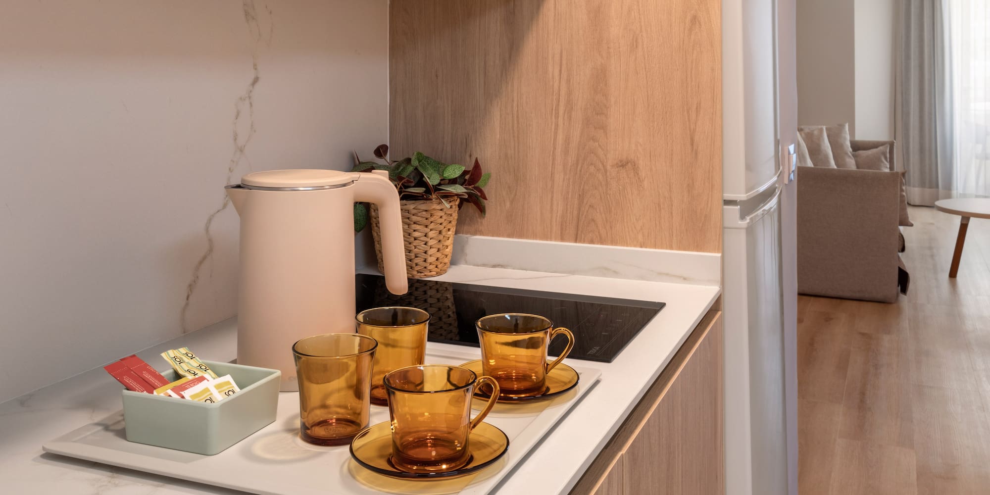 Modern studio apartment kitchenette with kettle, amber teacups, and coffee.