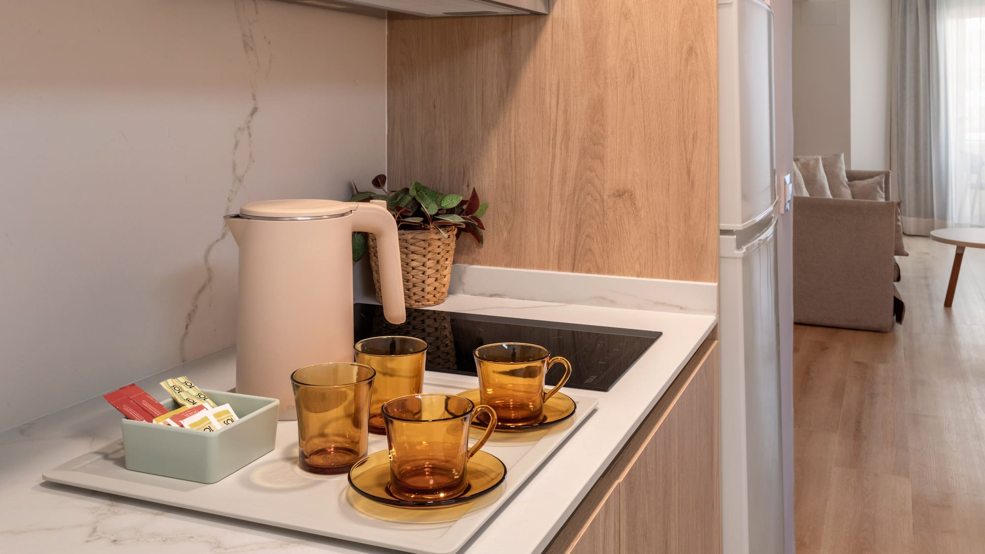 Modern studio apartment kitchenette with kettle, amber teacups, and coffee.