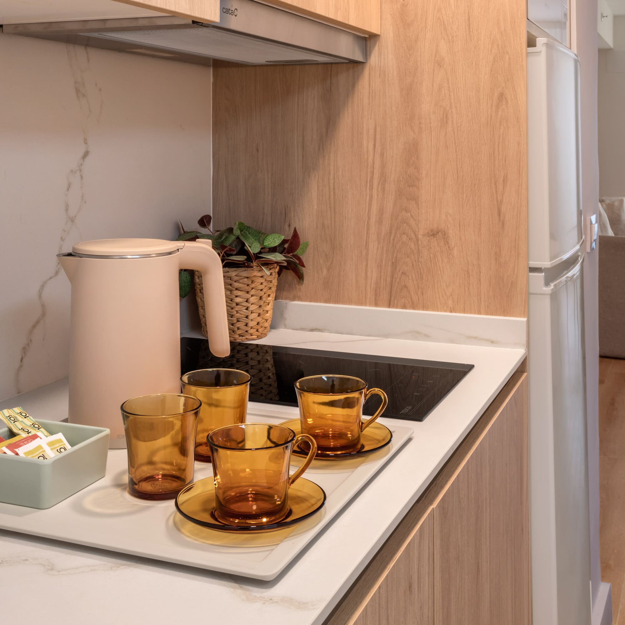 Modern studio apartment kitchenette with kettle, amber teacups, and coffee.