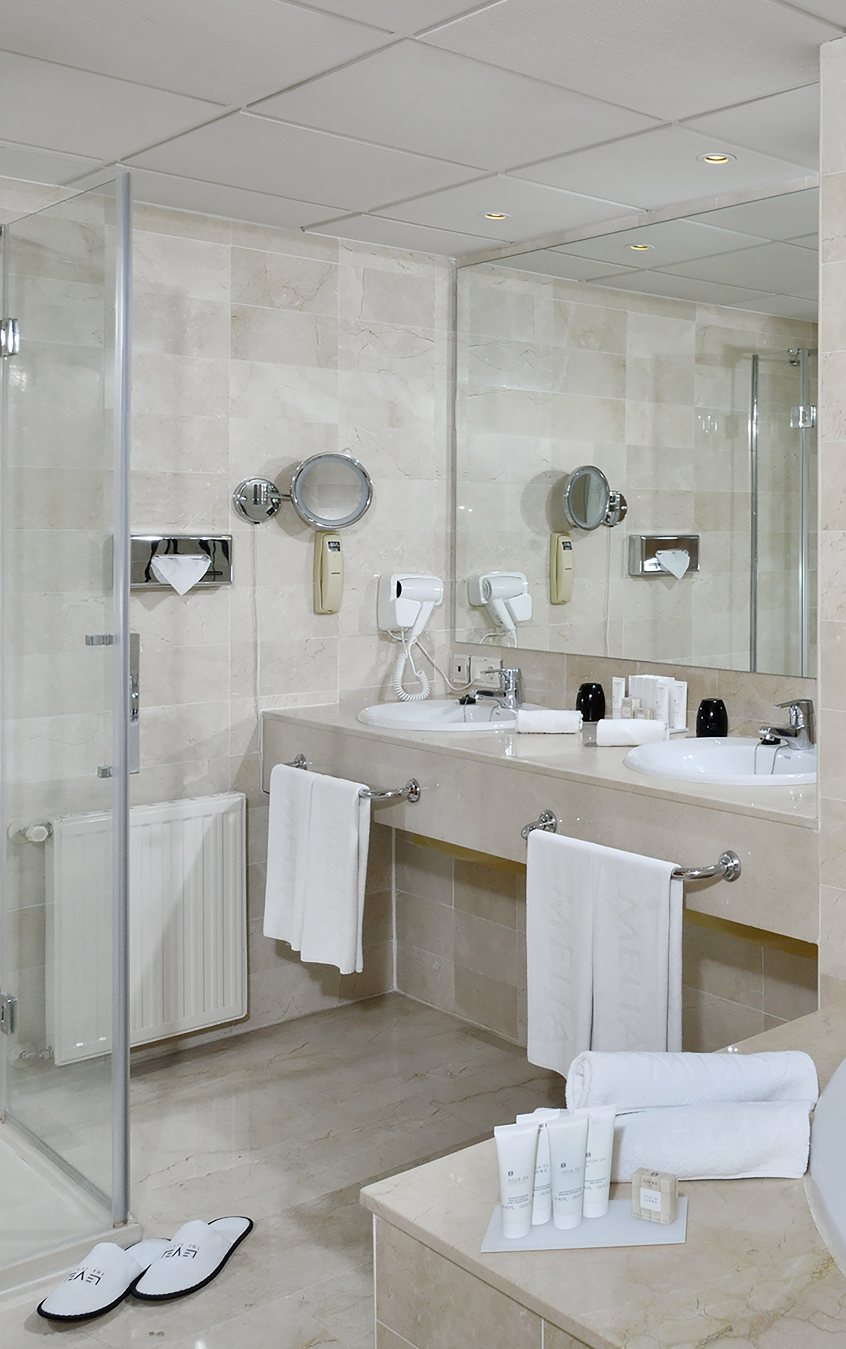 Luxurious marble bathroom with double vanity, large mirror, shower, and guest amenities.