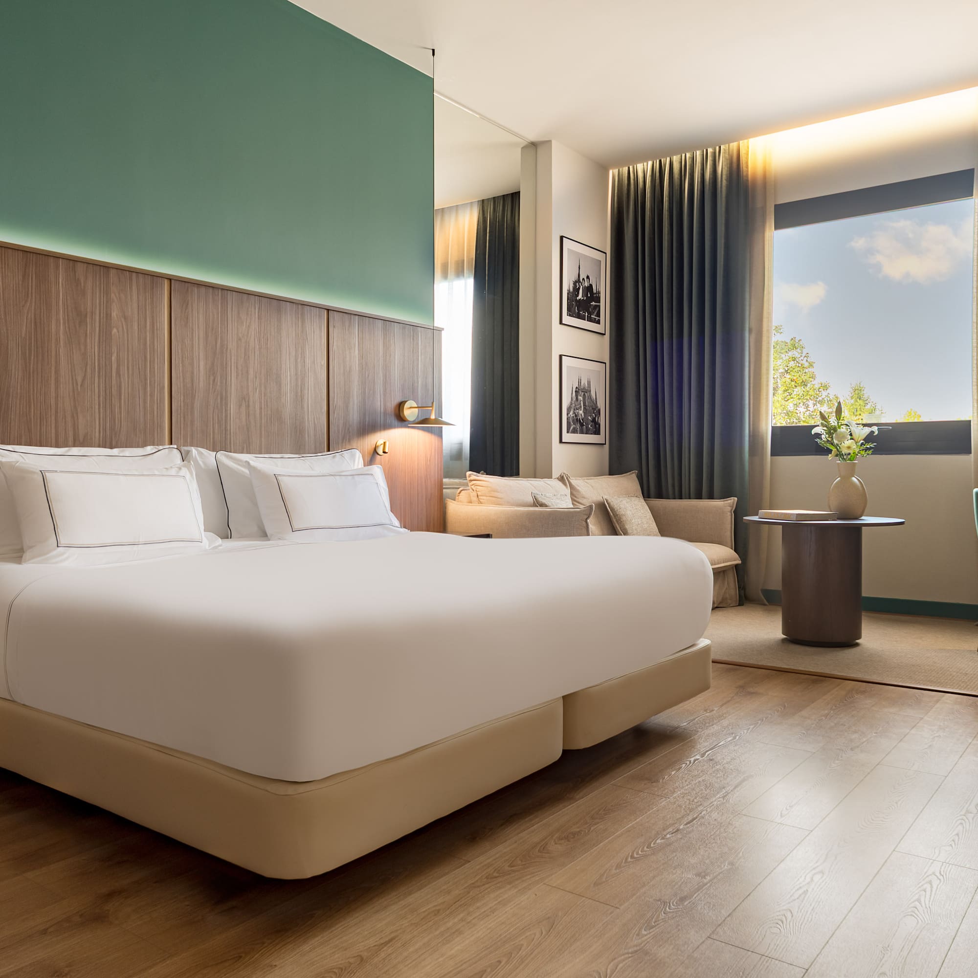 Modern guest room with king bed, green accent wall, wood floor, and large window.