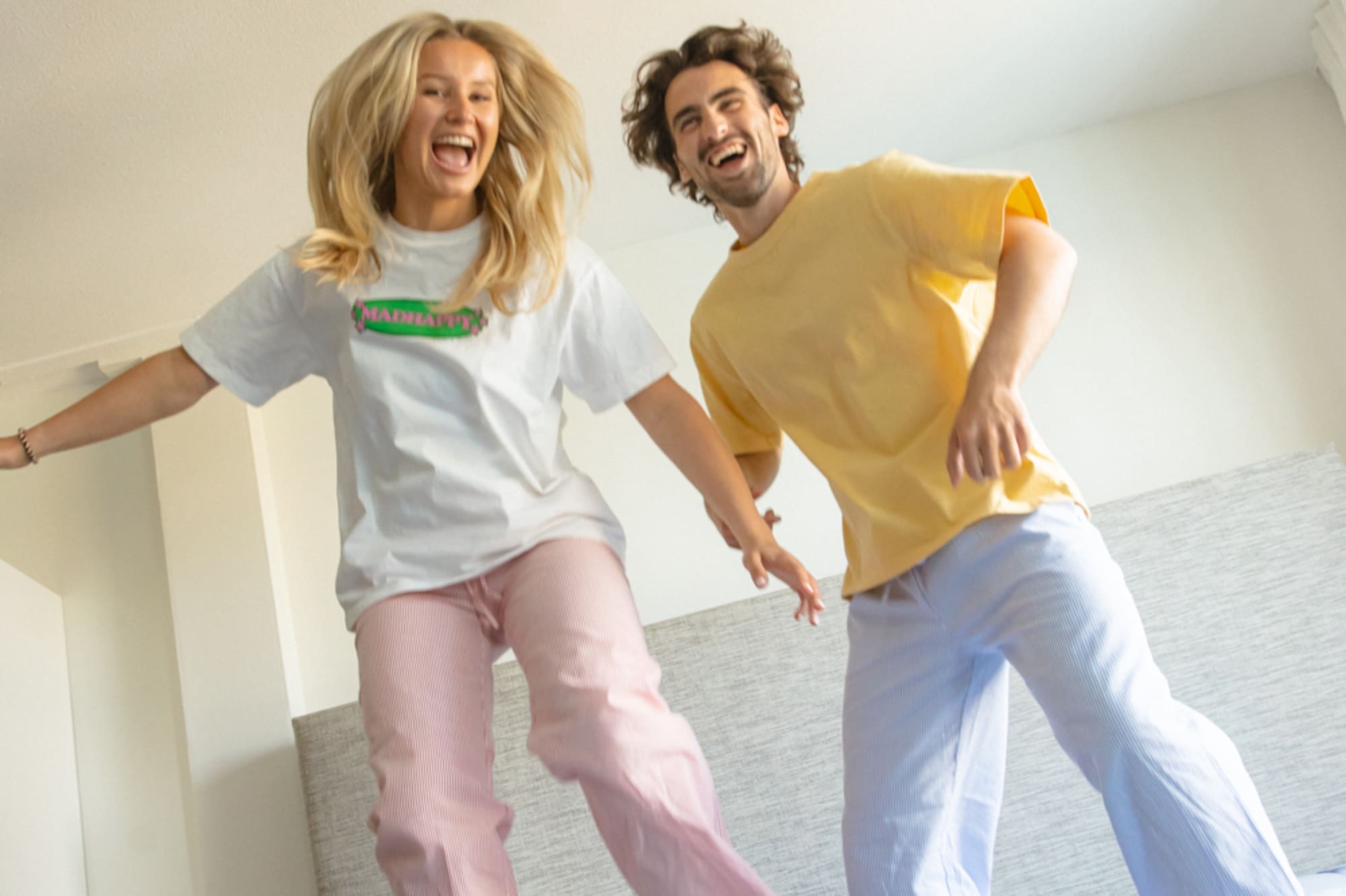 Joven pareja feliz saltando en la cama con pijamas en un dormitorio.