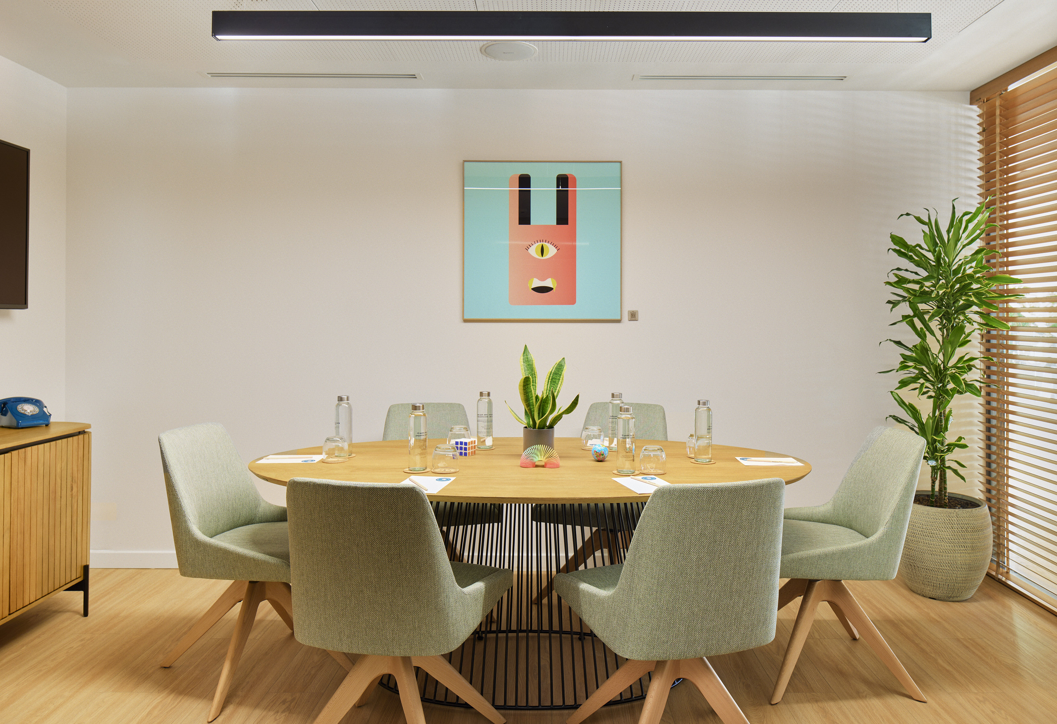 Contemporary meeting room with oval table, green chairs, and abstract art.