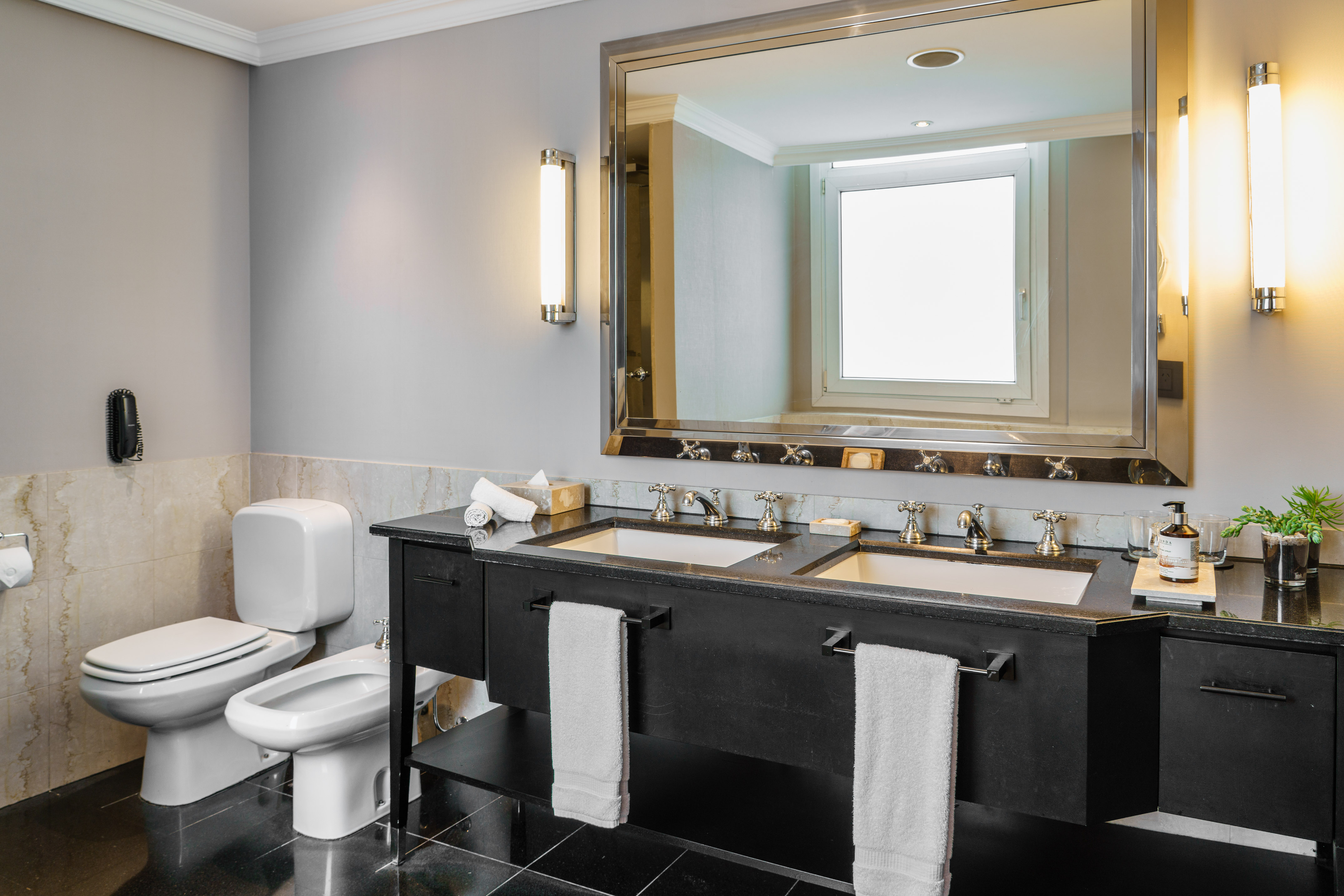 Luxury hotel bathroom with black double vanity, mirror, toilet, and bidet.