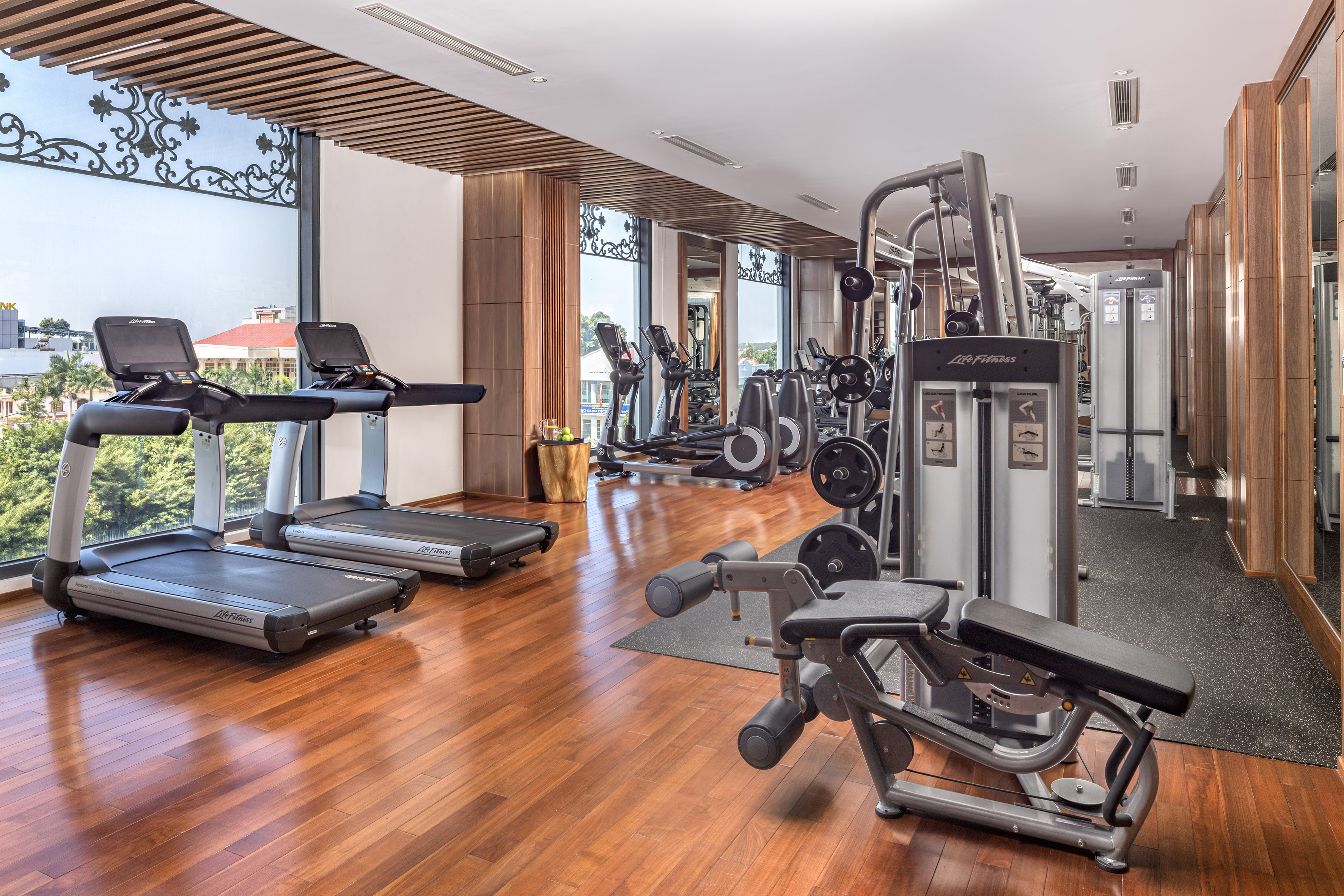 Bright modern gym with treadmills, weight machines, hardwood floor, and window views.