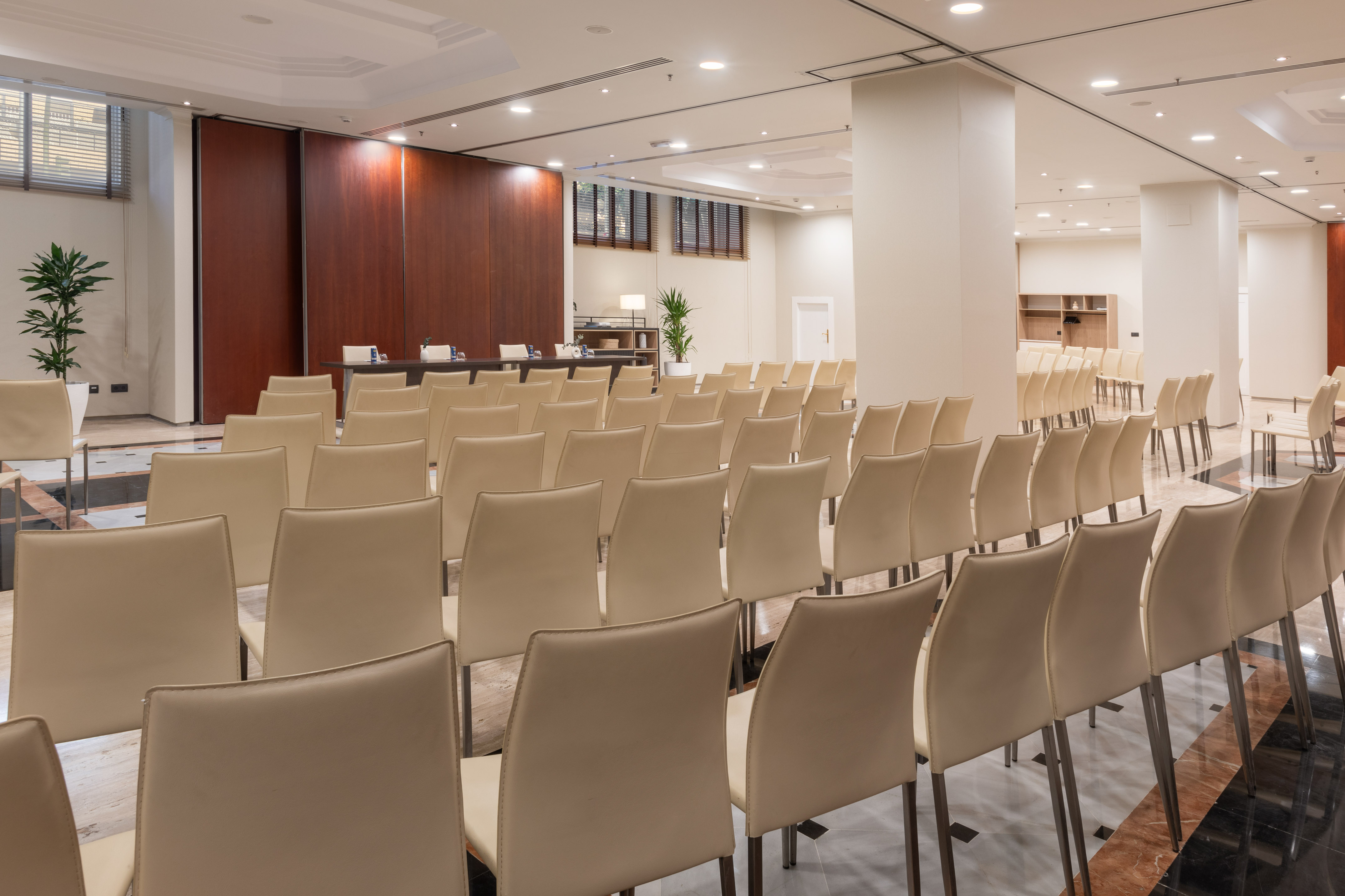 Empty conference room with rows of beige chairs and a dark wood presenter table.
