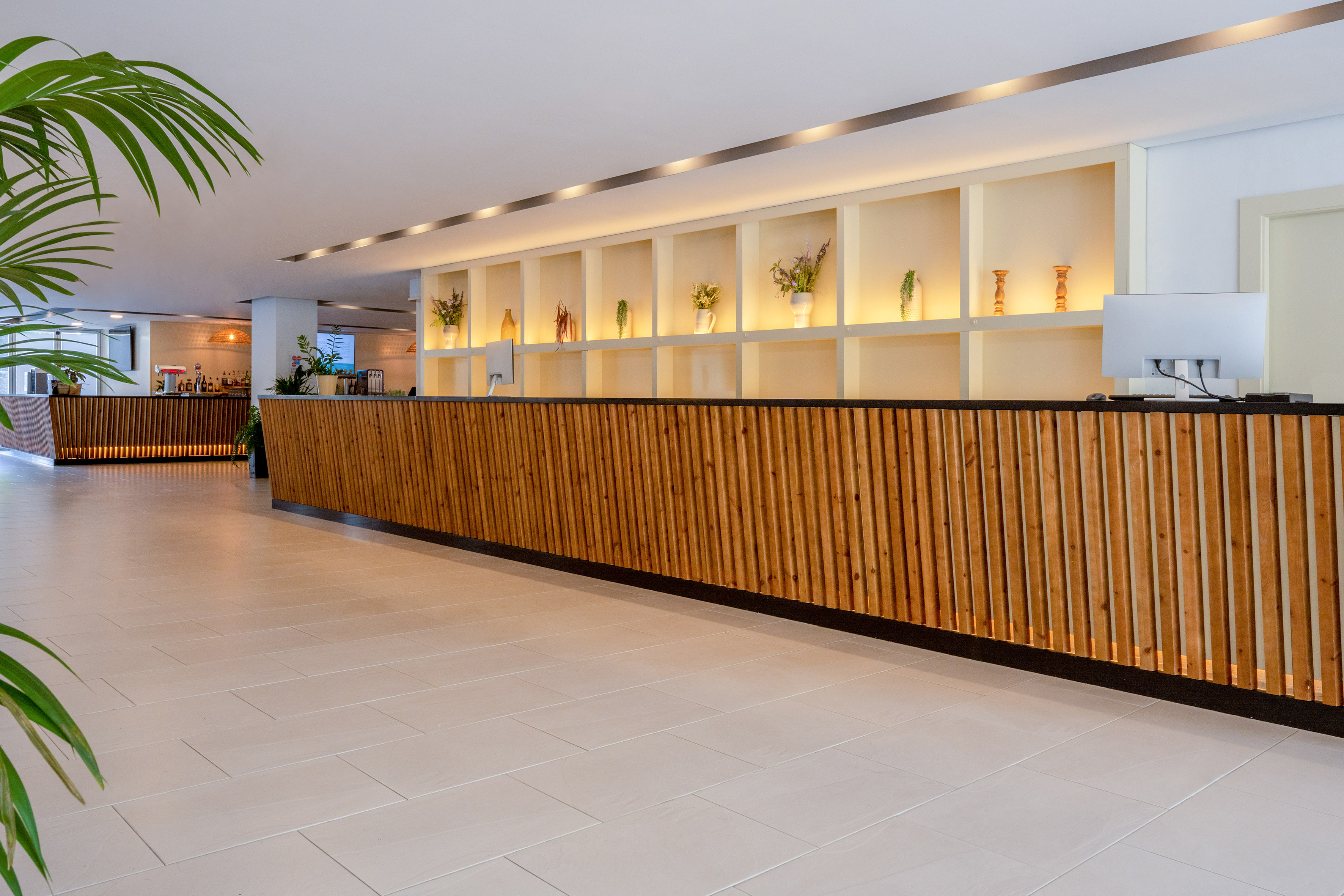 Hotel lobby with wood slat reception desk and backlit display shelves.
