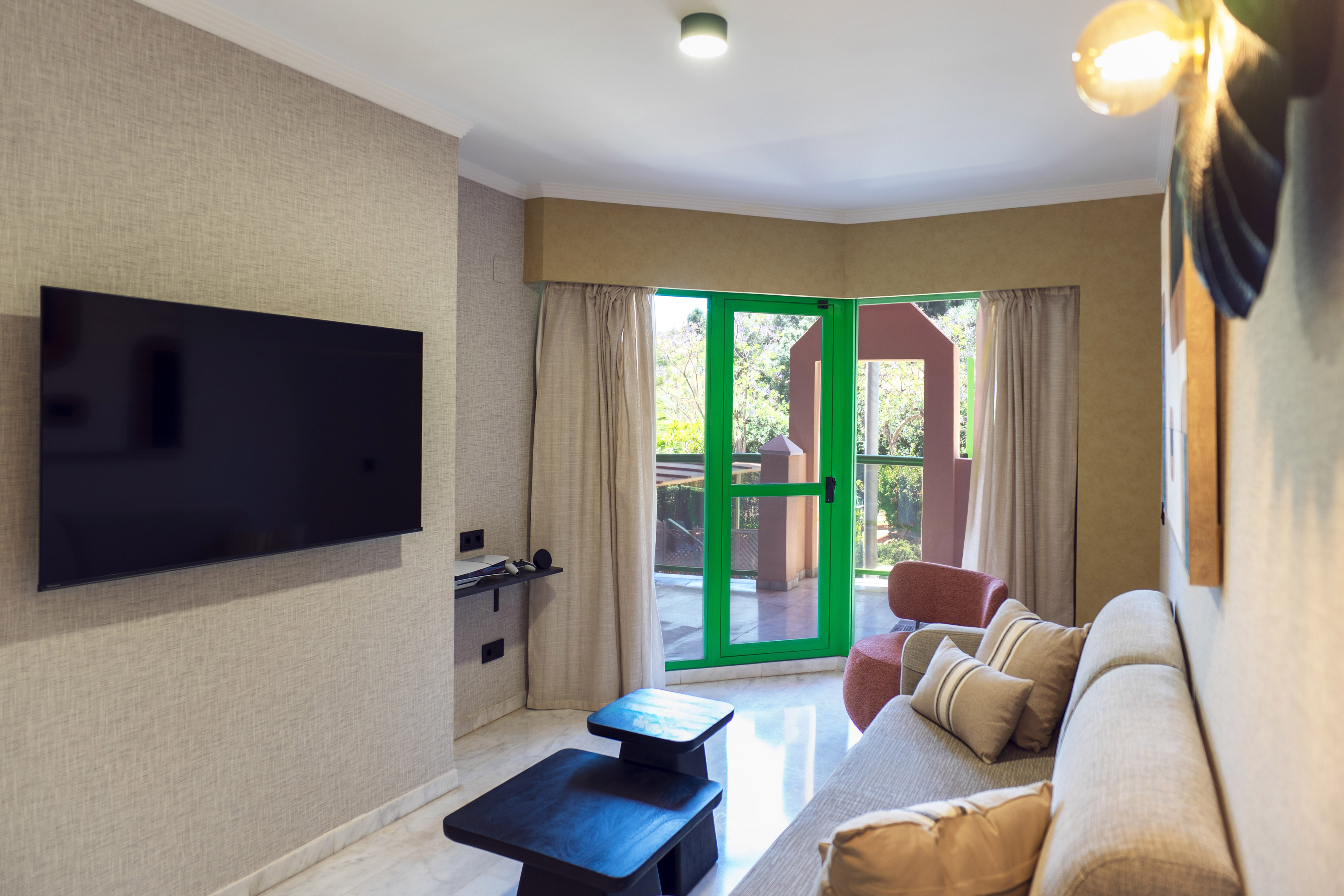 Modern hotel suite living room with TV, sofa, and green balcony doors.