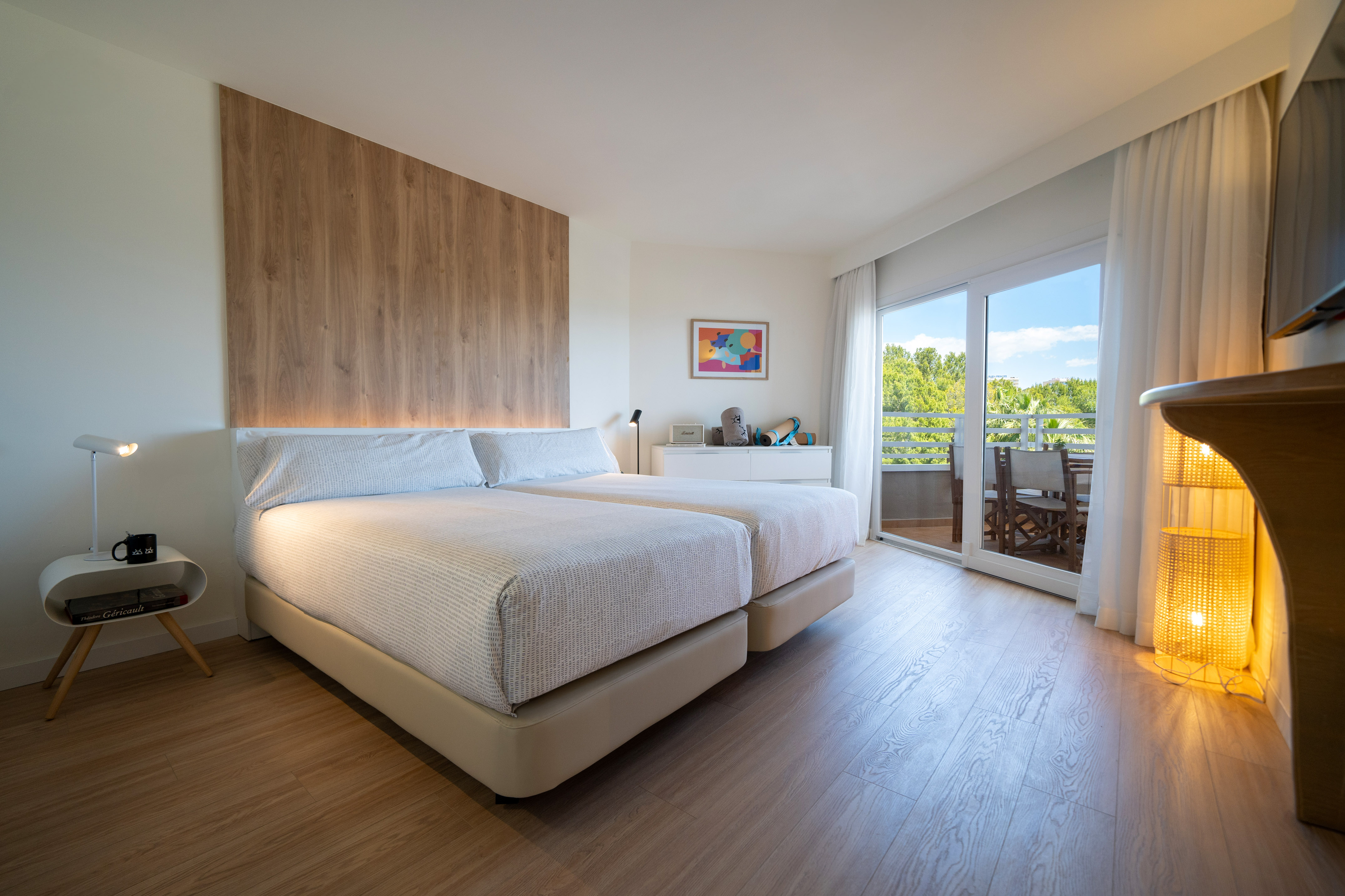 Modern hotel bedroom with twin beds, wood decor, and a sunny balcony view.
