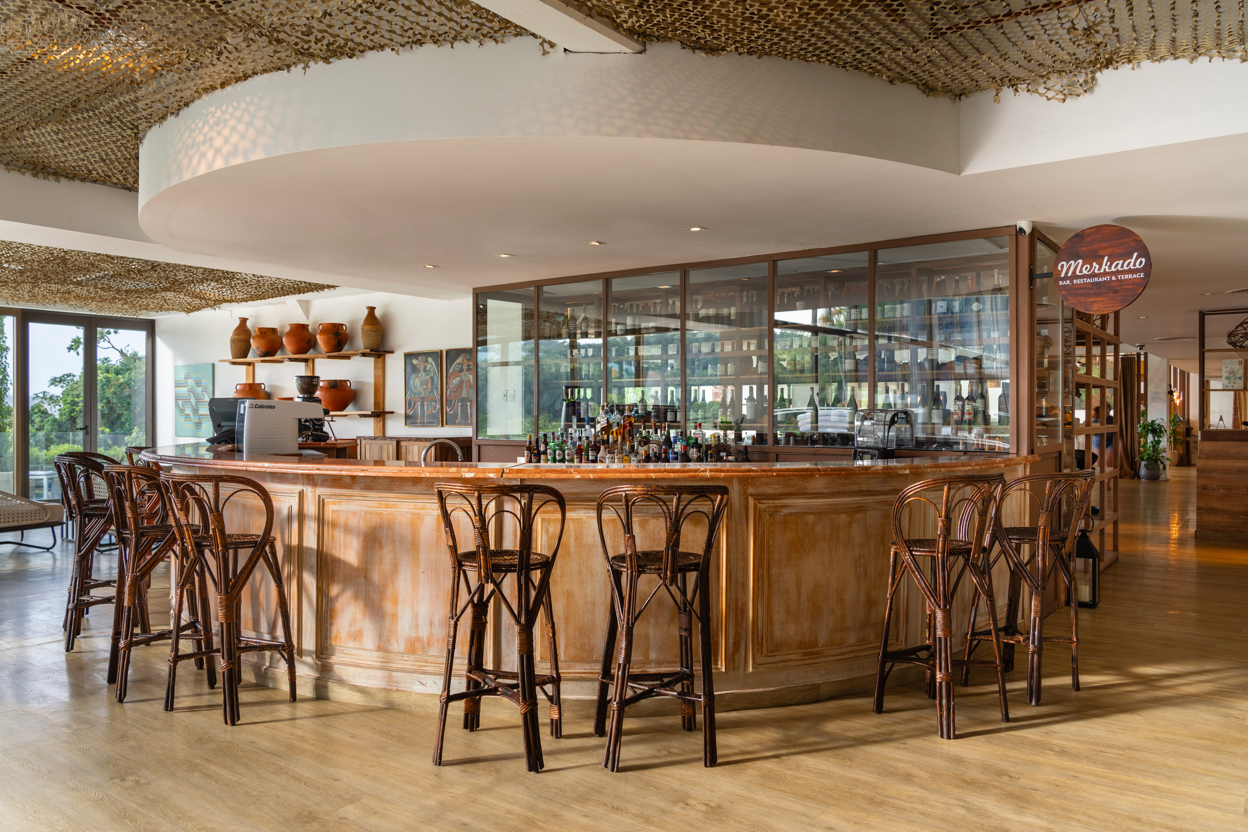 Merkado Bar interior: curved wooden counter, liquor display, rattan stools.