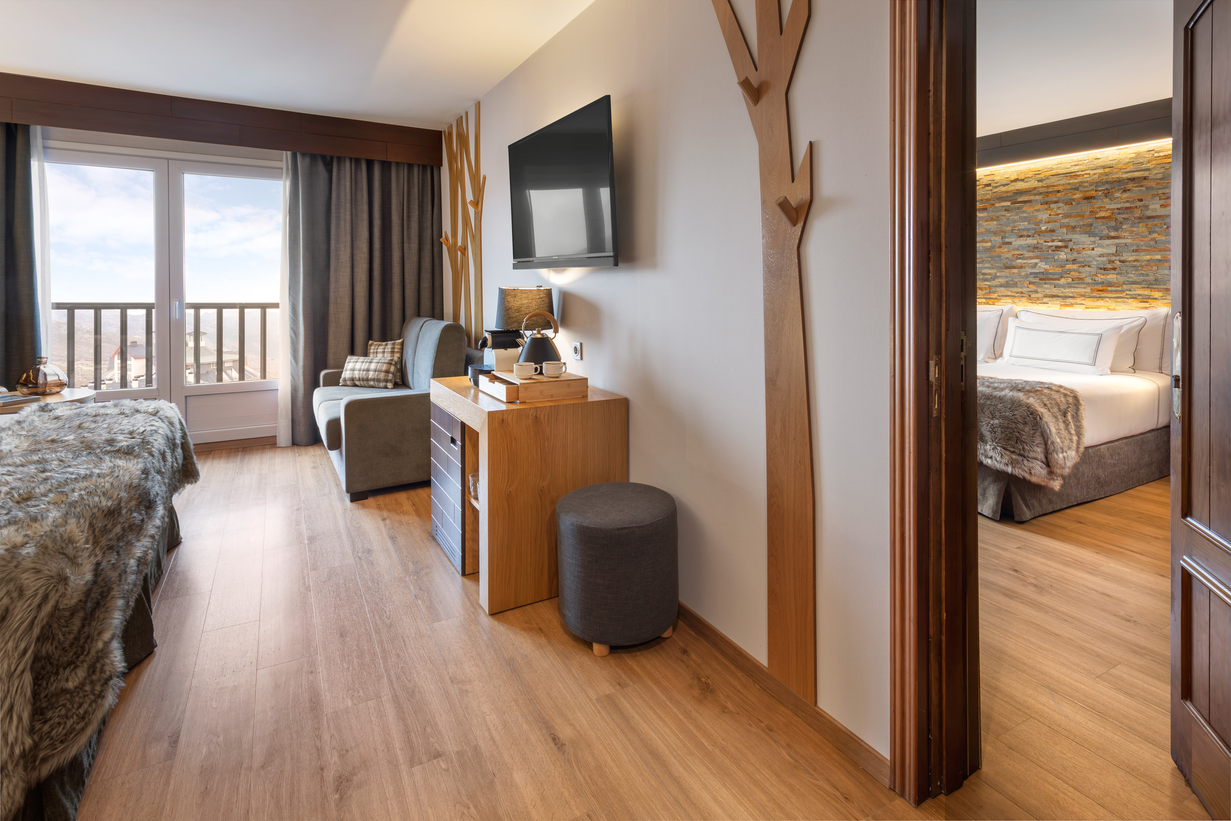 Modern hotel suite with living area, separate bedroom, and balcony mountain view.