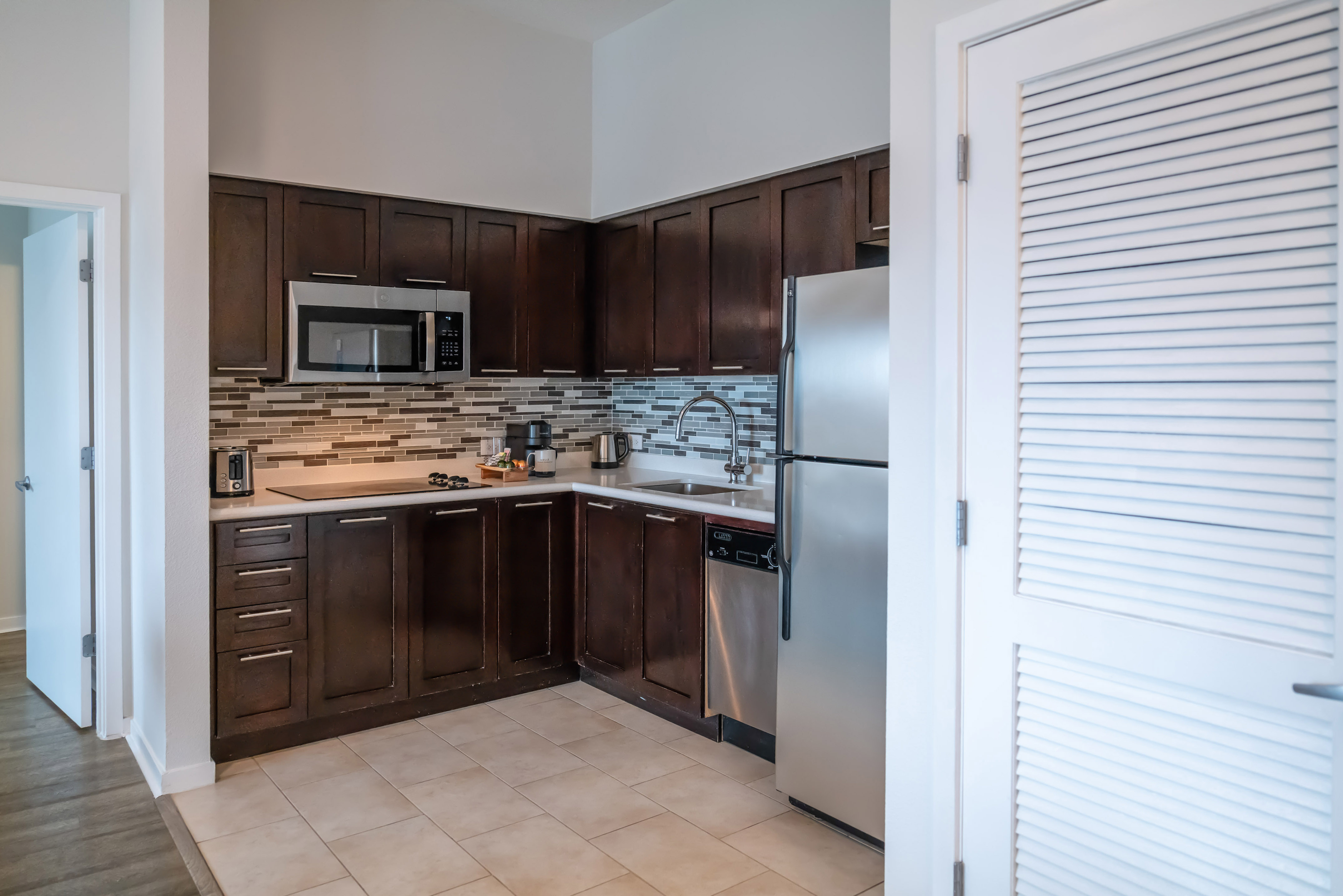 Modern apartment kitchen with dark cabinets, stainless appliances, tiled floor. - The Level One Bedroom Suite - Meliá Orlando Celebration, Orlando