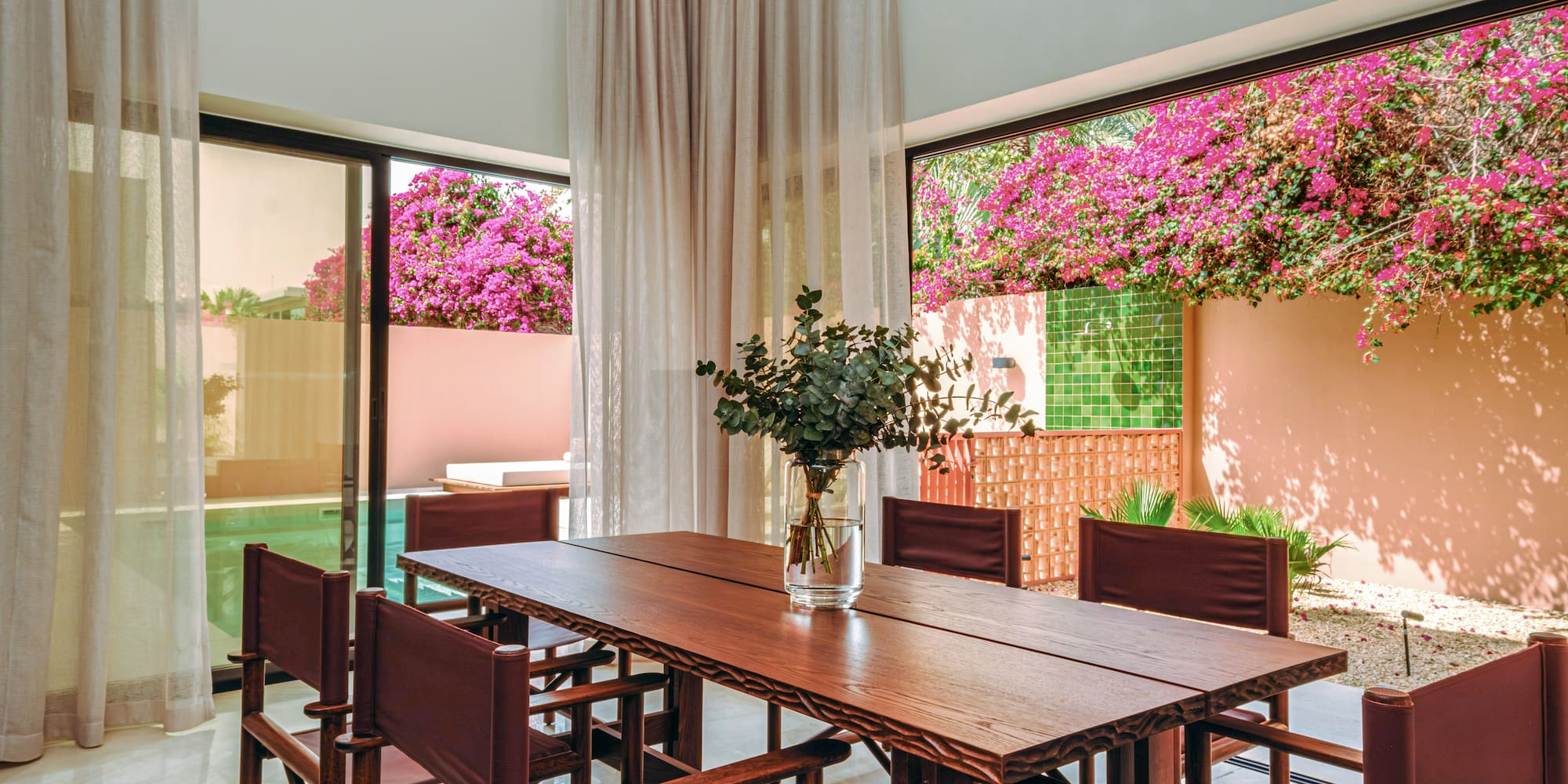 a table with chairs and a vase of flowers in front of a window