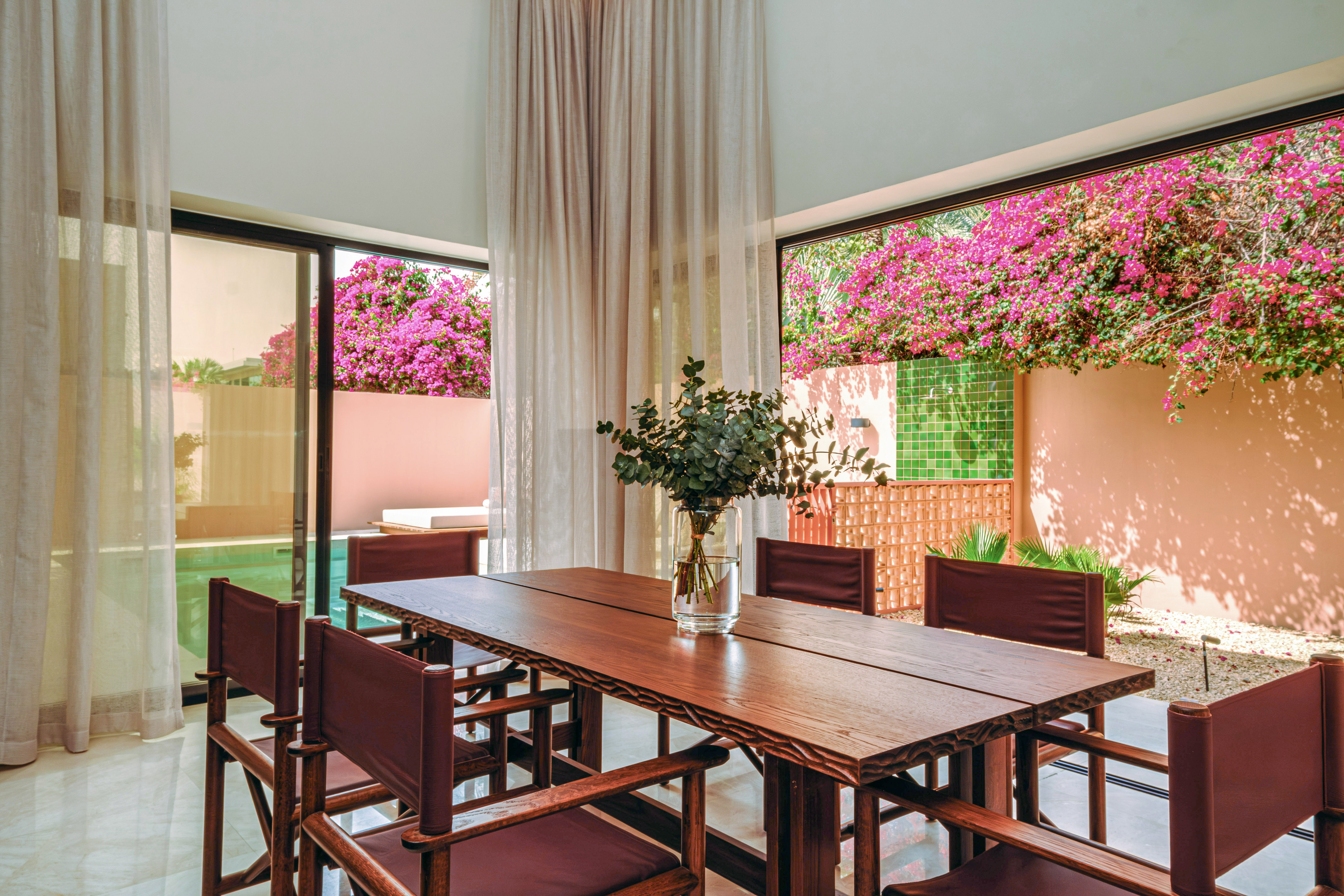 Dining room, wooden table, chairs, bougainvillea, pool view from windows.